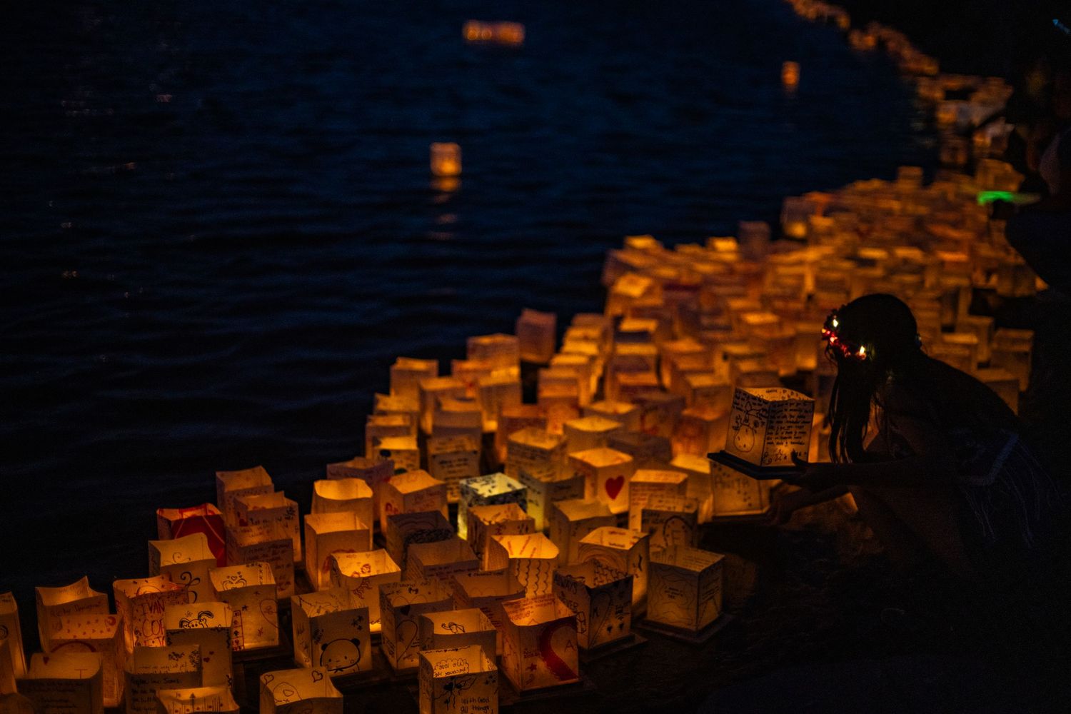 Glowing paper lanterns float on dark water at night, as a person releases them in a serene lantern festival.