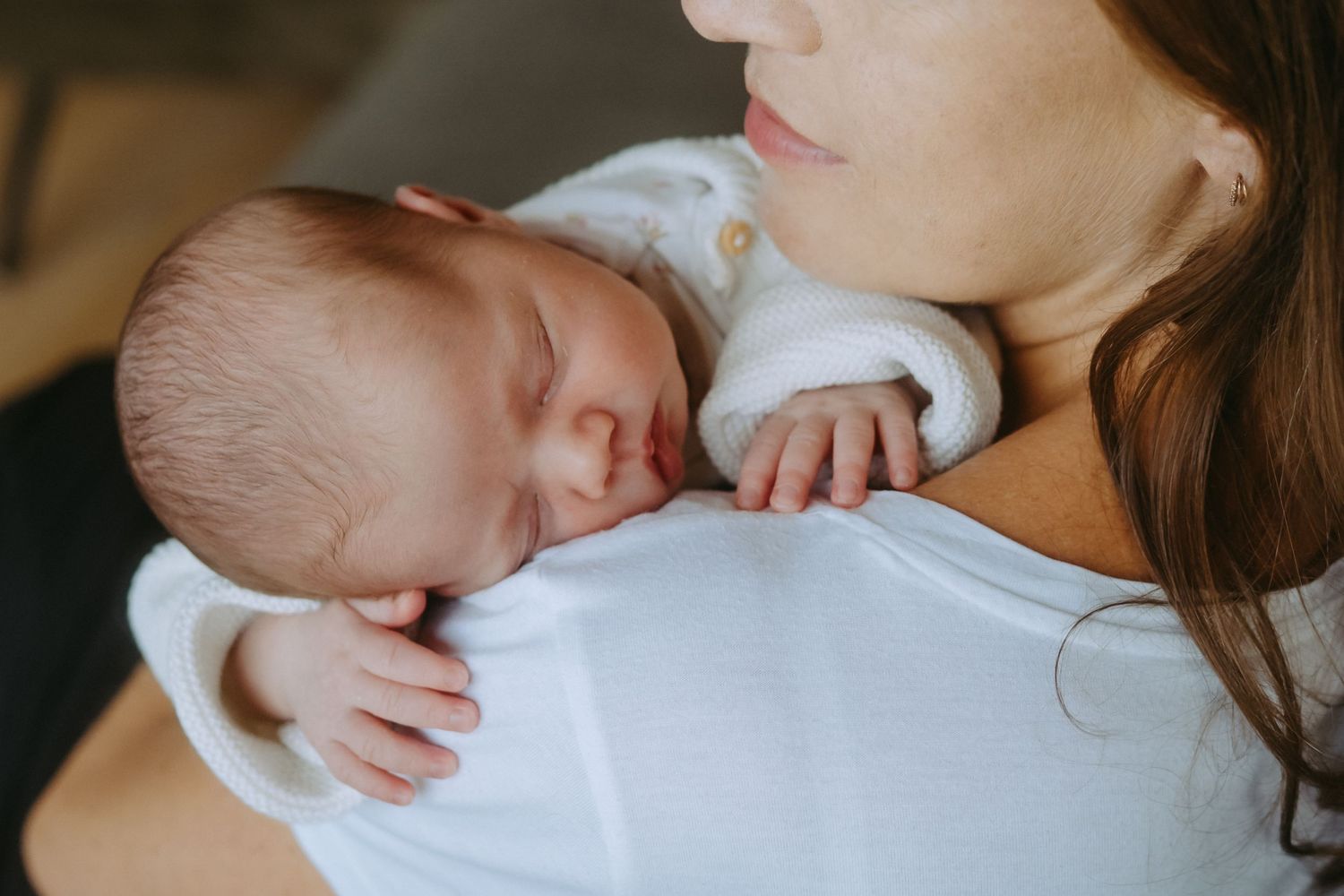 Newborn baby sleeping peacefully on mother's shoulder in a tender close-up portrait.