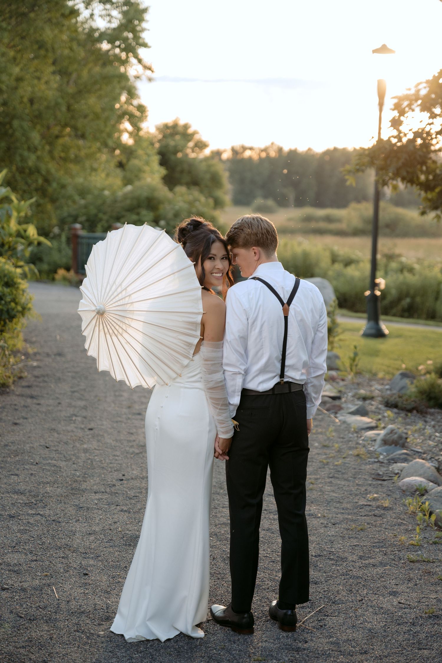 bride and groom hold hands, bride looks back at the camera during sunset wedding portraits in Hudson, WI.