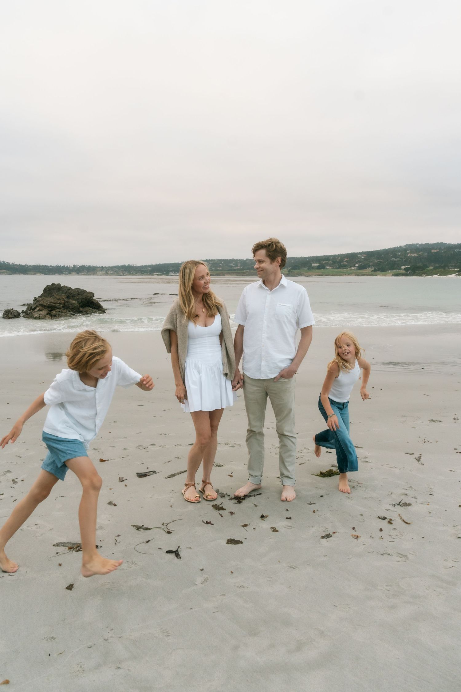 Family of four enjoying a fun day on the beach, with parents smiling and children playing on sandy shore.