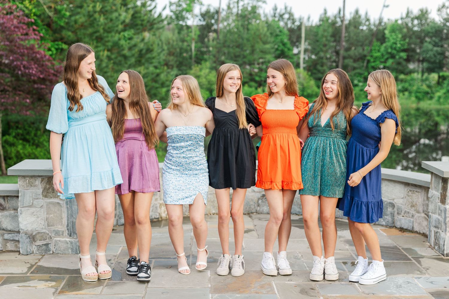 Group of friends in colorful summer dresses standing together on stone patio.