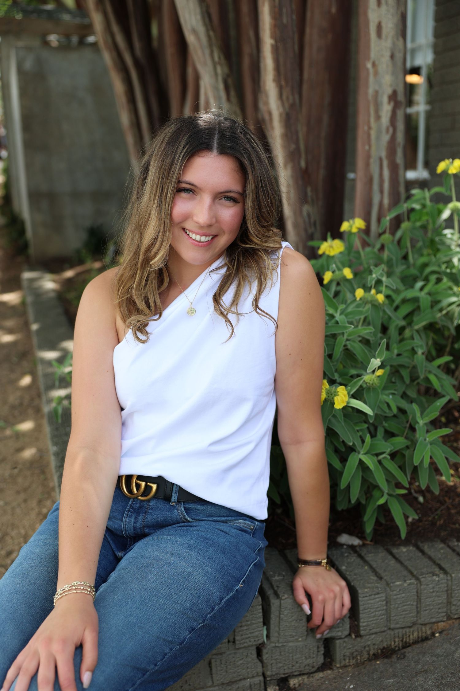 Casual outdoor portrait featuring white one-shoulder top and designer belt against garden background.
