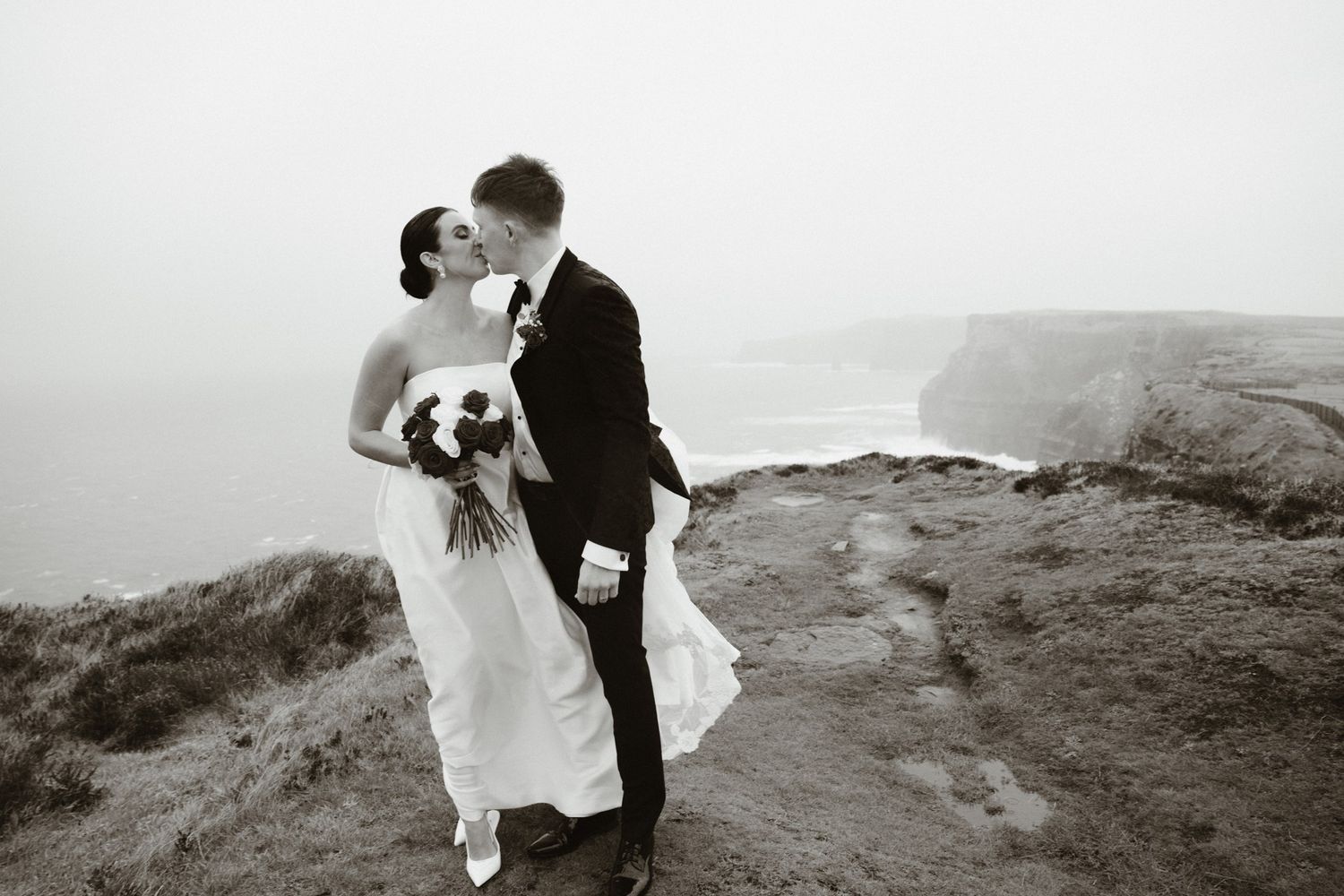 Aisling and Hugh kissing beside the cliffs and sea on their wedding day in Doolin.