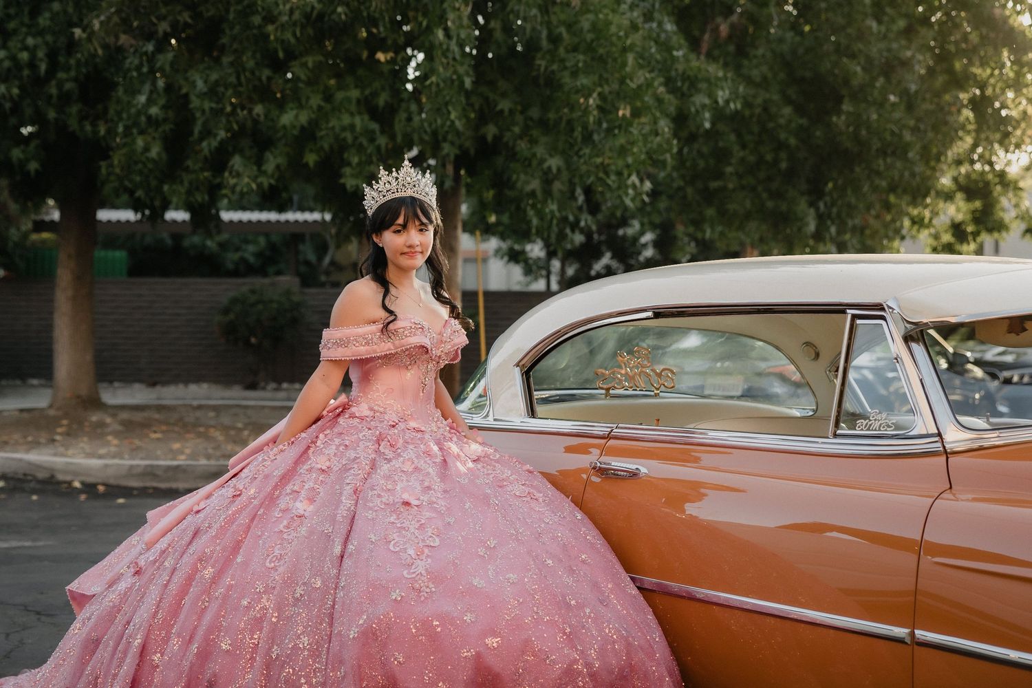 Young woman in a red ball gown and crown poses among roses for a quinceañera portrait.