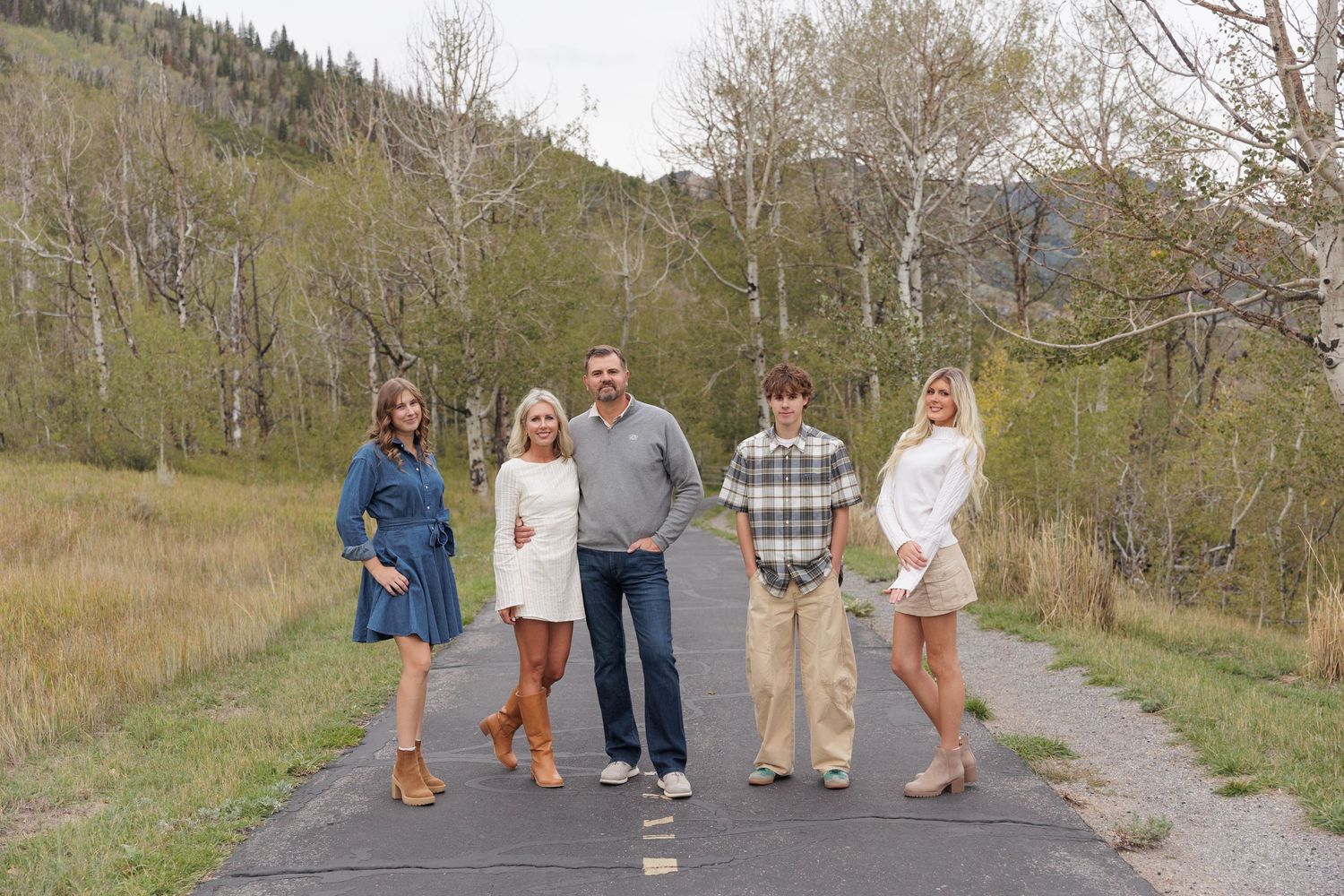 Family of five poses on a paved path surrounded by autumn trees and mountain landscape.