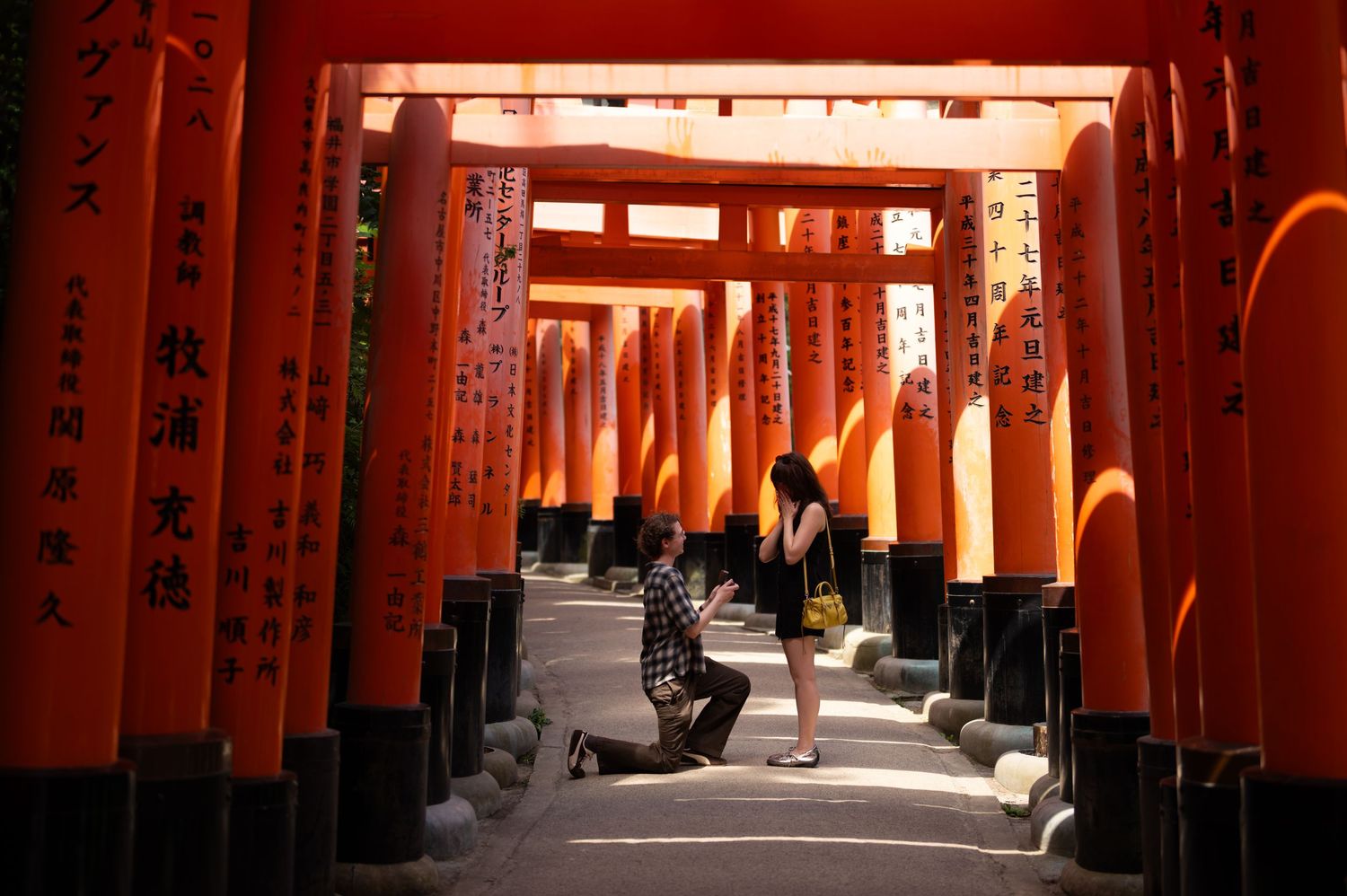 Man kneeling on one knee proposing to a woman among the vermilion torii gates at Fushimi Inari Shrine in Kyoto, Japan.