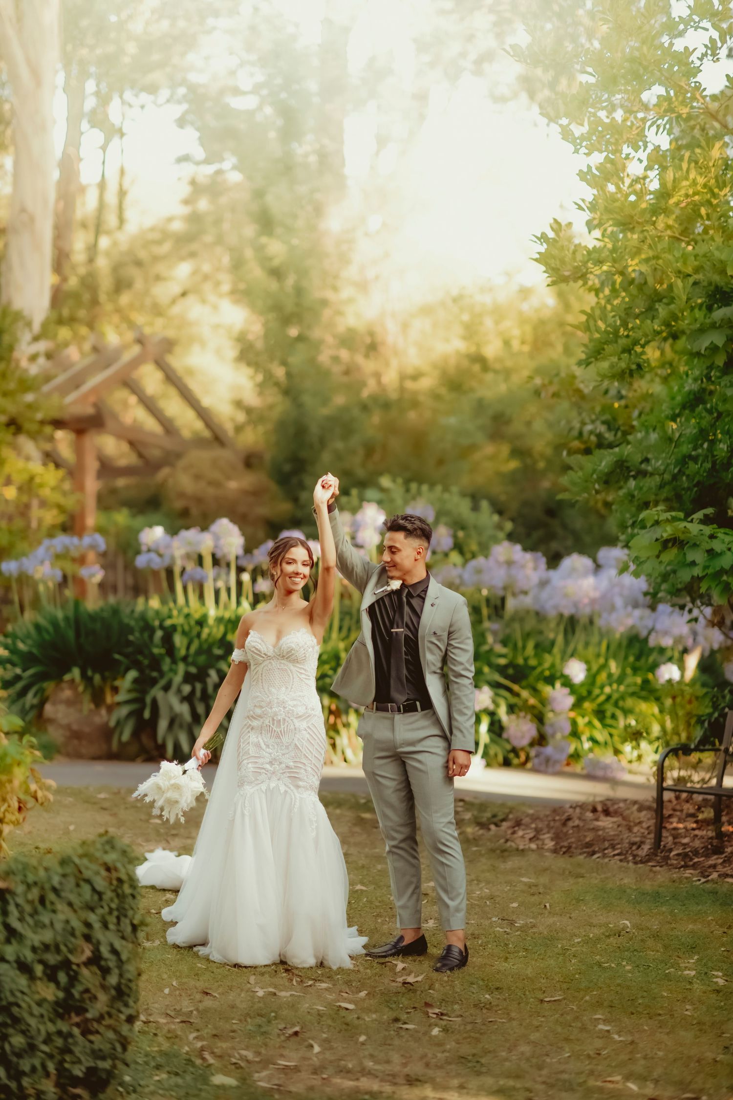 A couple celebrates at their garden wedding surrounded by purple flowers and greenery in golden afternoon light.