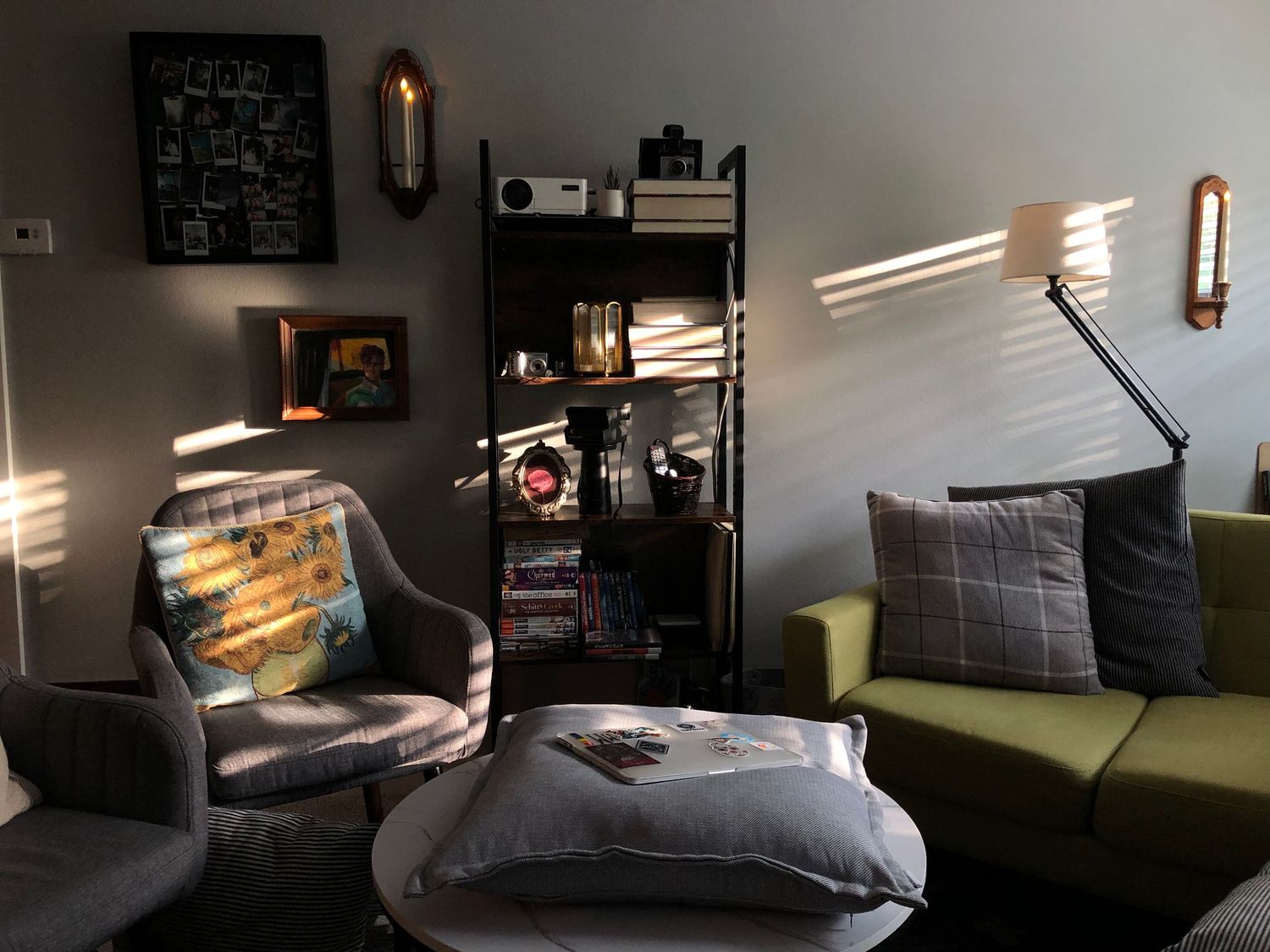 organized shelf with sunlight thought the blinds in a living room, seats, throw pillows and laptop.
