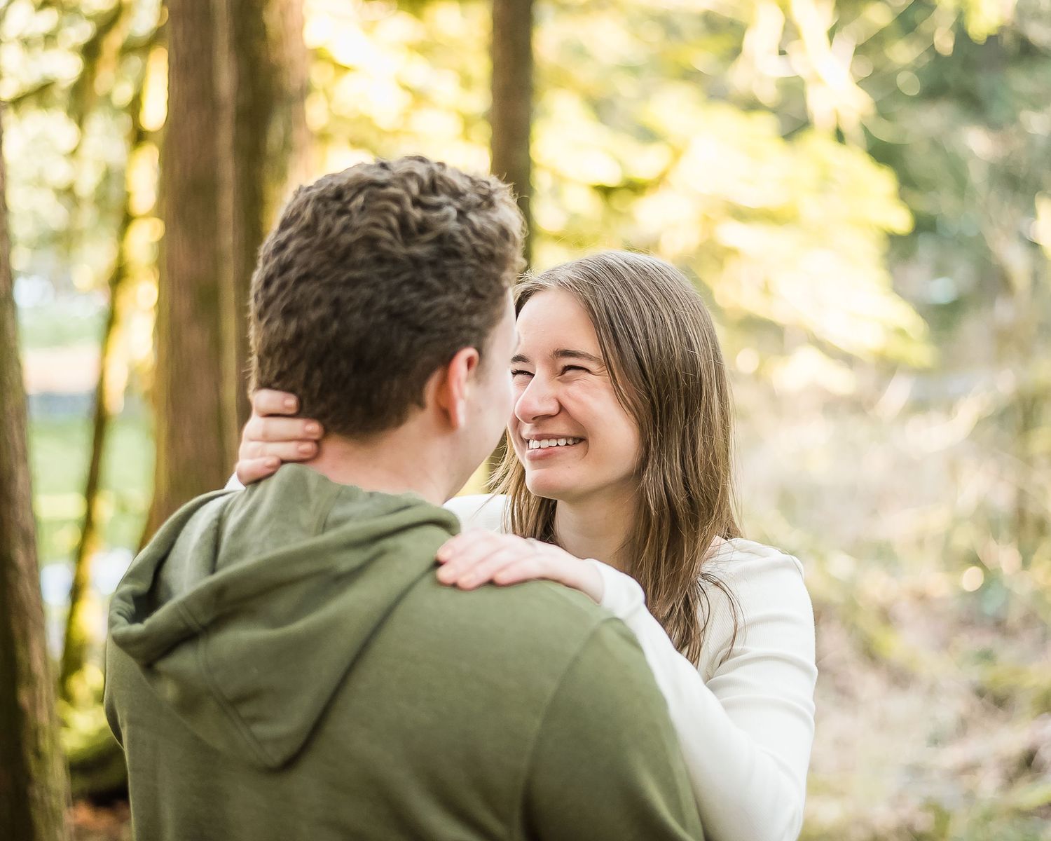 A woman smiles brightly at her fiance during their engagement session in the forest.