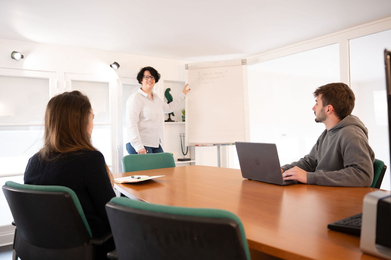 Une cheffe d’entreprise anime une réunion stratégique devant deux collaborateurs, illustrant la dynamique d’équipe en PME.