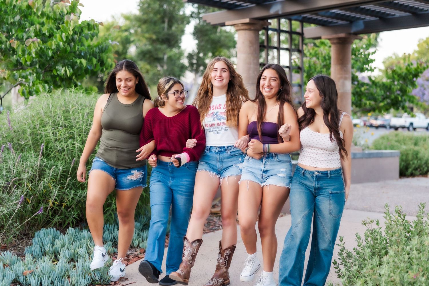 Group of friends spending time together outdoors while sitting and laughing against a garden backdrop.