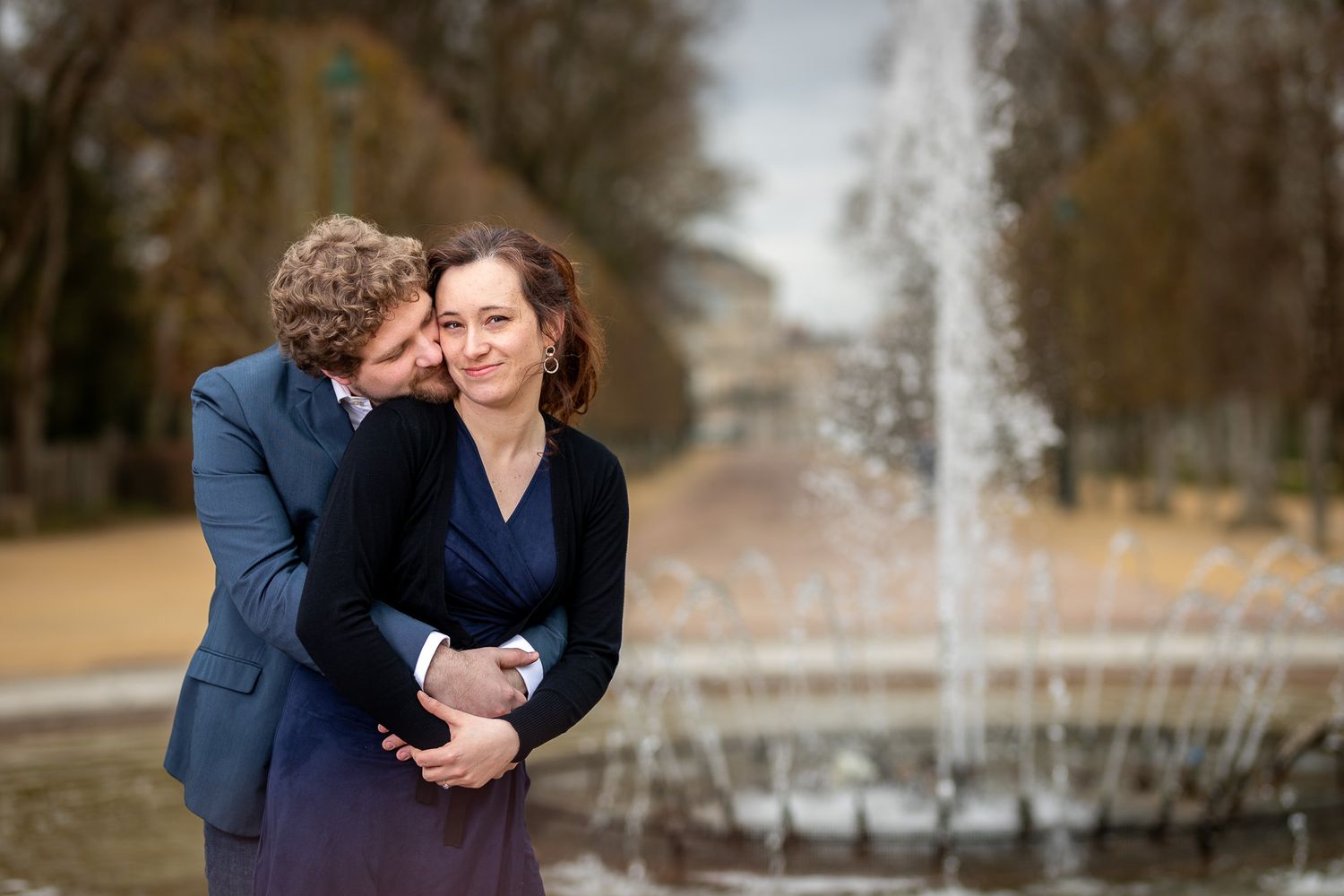 A tender moment between two people near a fountain in a park.