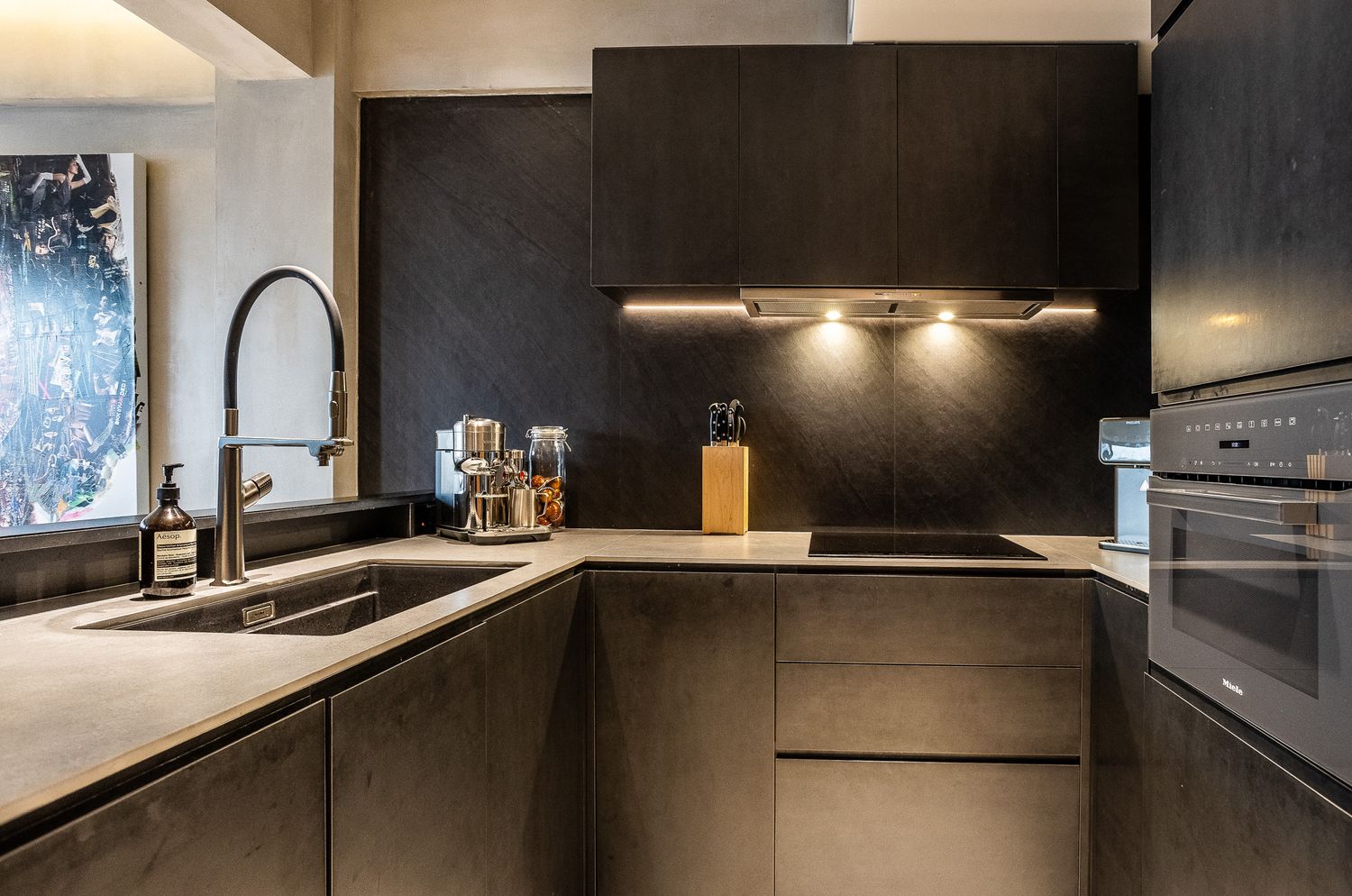 Modern dark kitchen with U-shaped layout featuring matte black cabinetry, undermount sink, and built-in stainless steel oven.