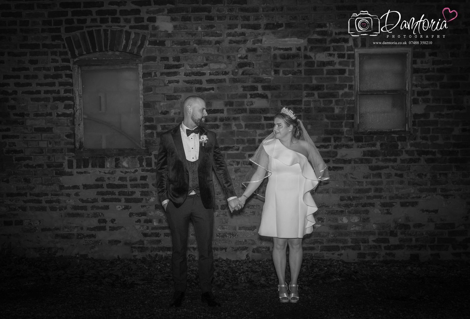 Romantic silhouettes of a wedding couple against a dramatic brick wall background.