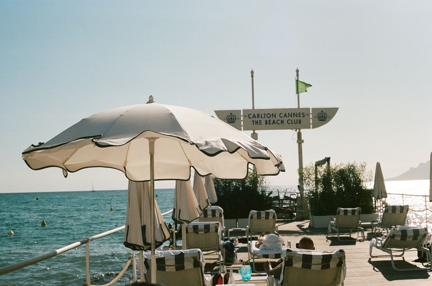 White beach umbrellas and lounge chairs line an oceanfront deck on a sunny Mediterranean seaside.