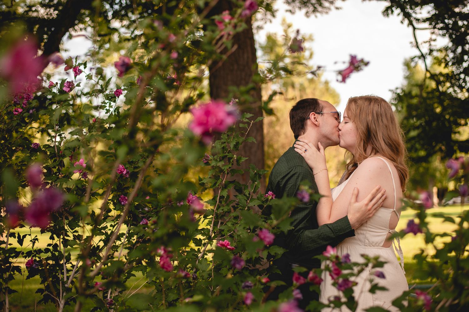 Romantic moment captured between couple surrounded by pink blooming flowers in evening light.