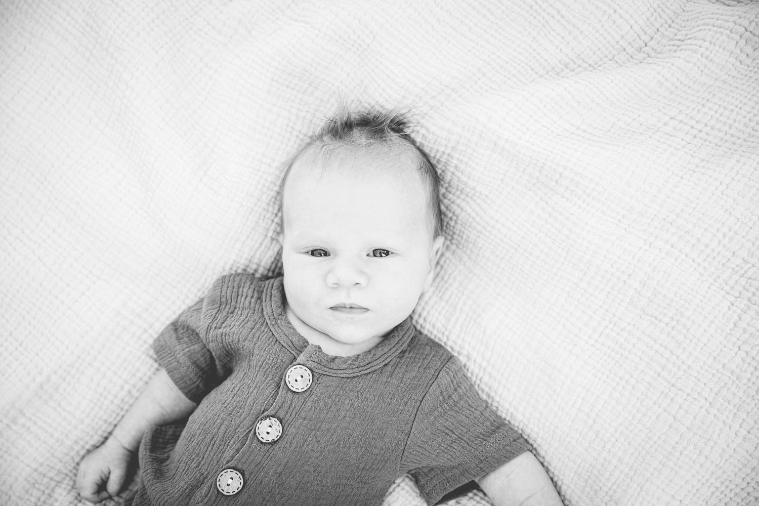 newborn baby laying on a blanket and looking straight at photographer