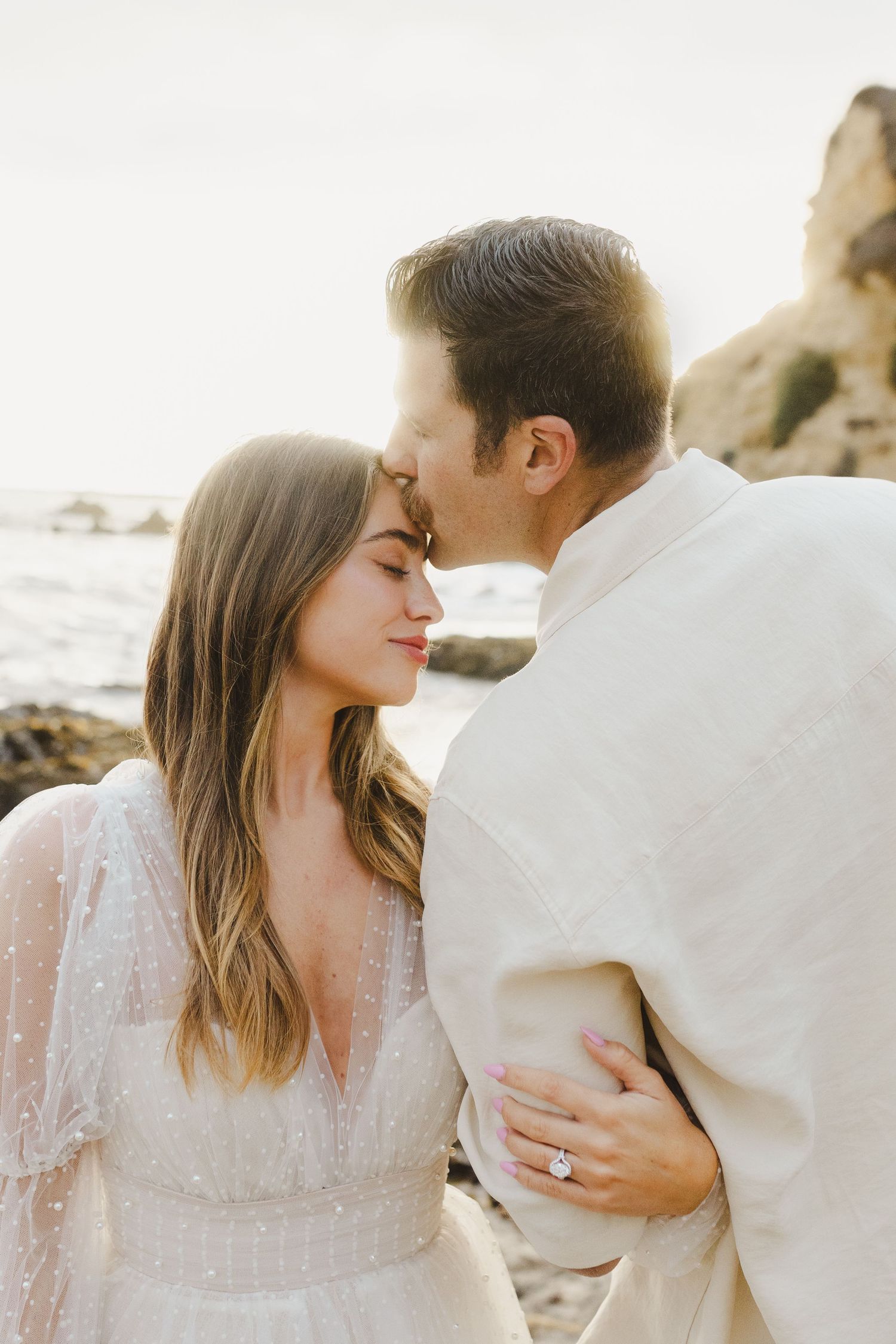 Romantic couple in white embraces on a beach at sunset in a series of intimate portrait photographs.