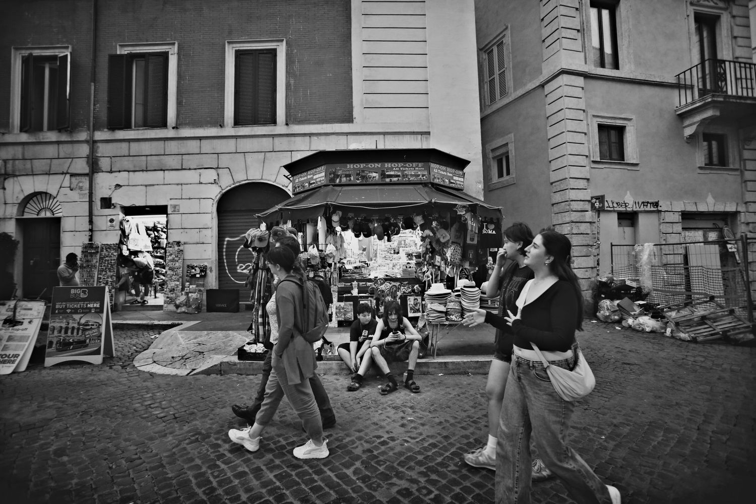 A black and white street scene shows people gathered outside a small storefront in an Italian city.