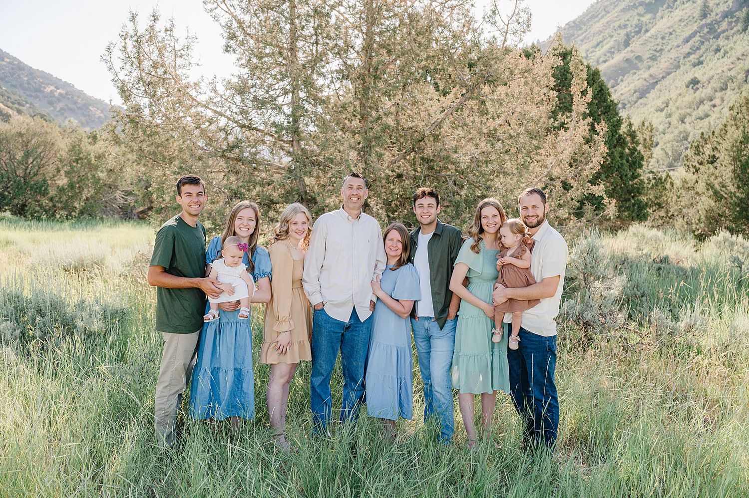 A group portrait of family members wearing coordinated outfits standing in a mountain meadow at sunset.