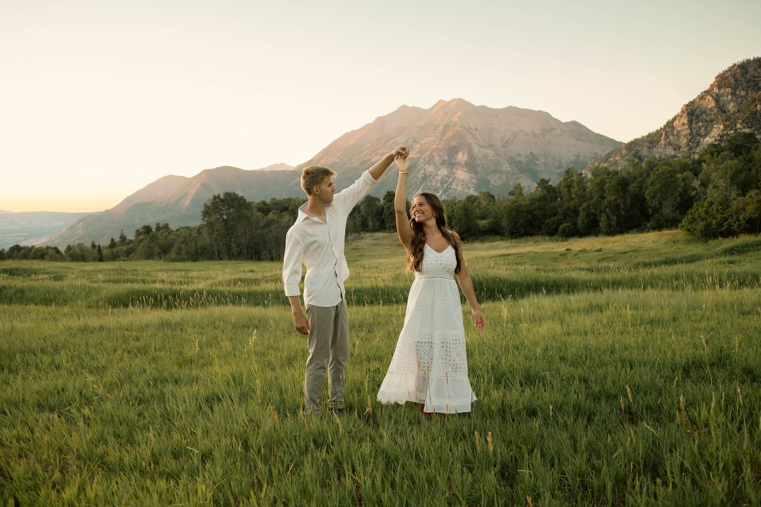Dancing couple celebrates in mountain meadow during golden hour.