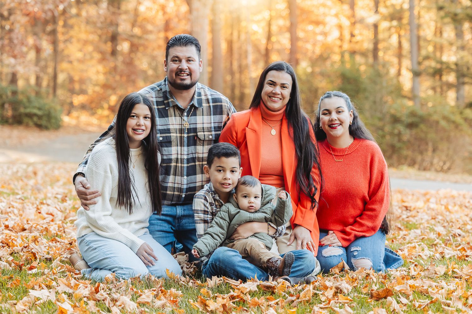 Family sitting together on autumn leaves during an outdoor photo session.