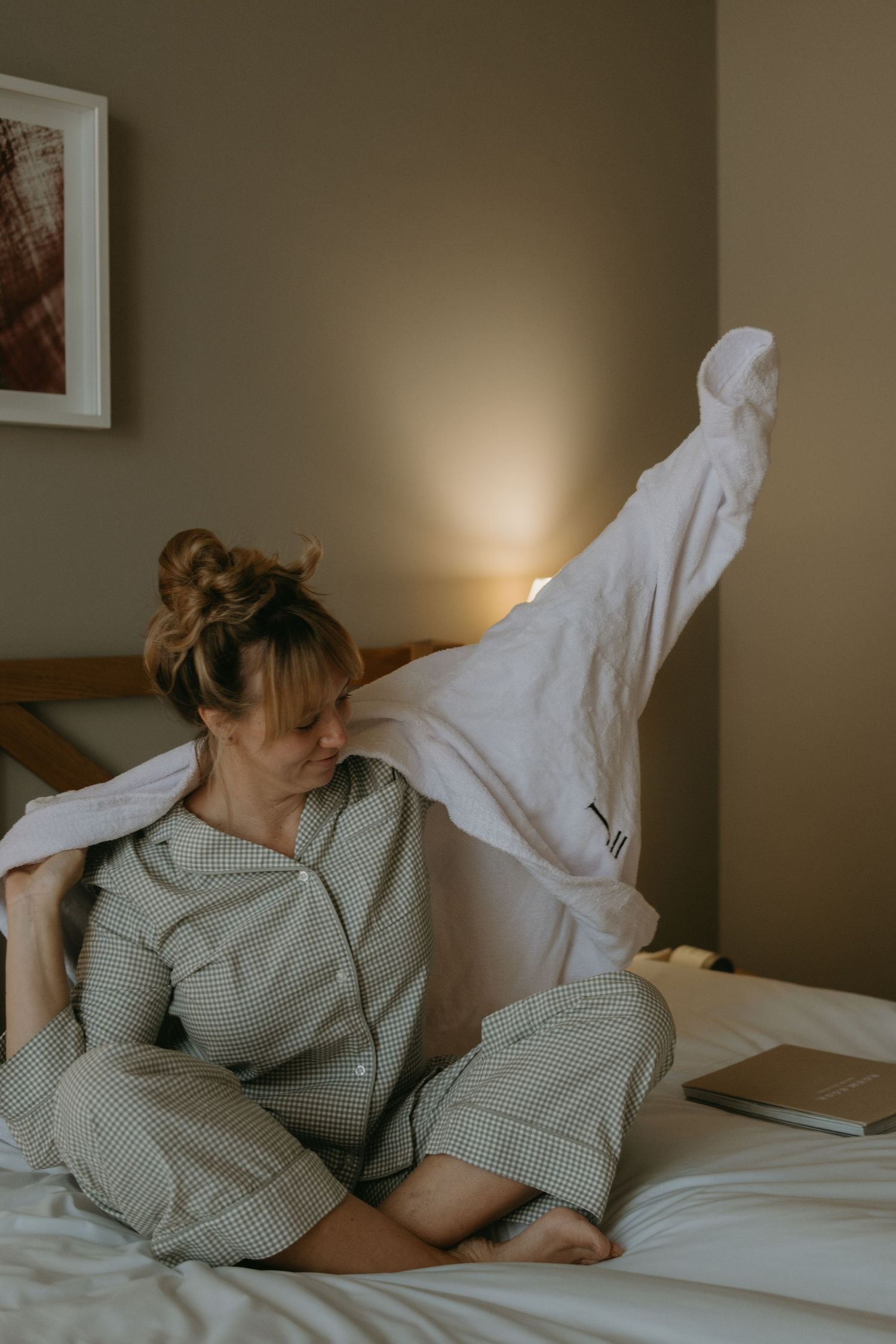 a woman sitting on hotel bed putting on bathrobe while being captured by brand photographer in Stockholm
