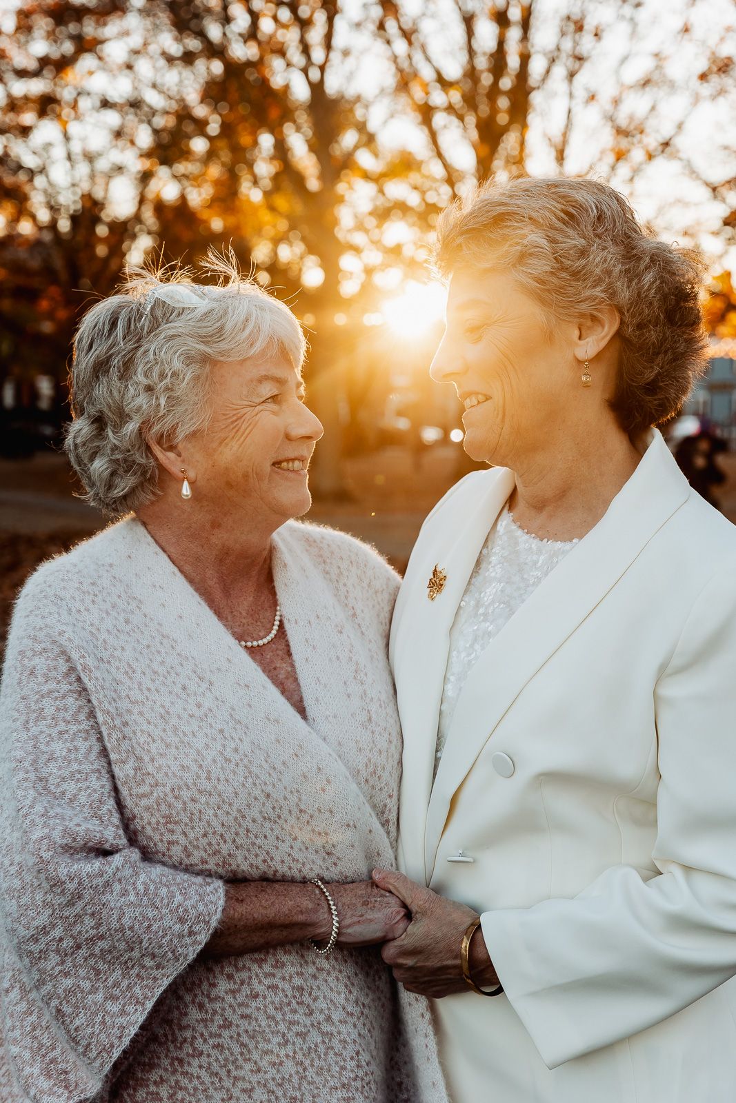 Tender moment between two people at sunset with golden light filtering through autumn trees.