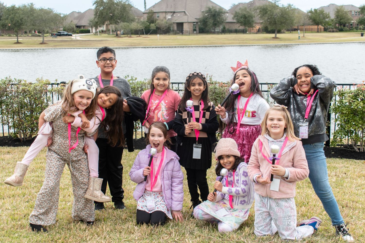 A group gathered outdoors by a pond poses together wearing pink party attire.