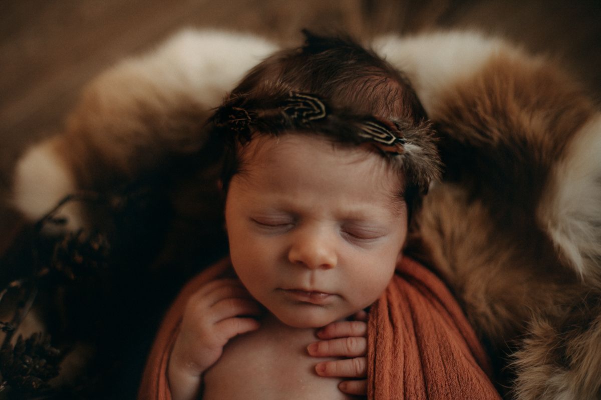 A peaceful newborn baby swaddled in cream colored fabric rests against a textured gray background.