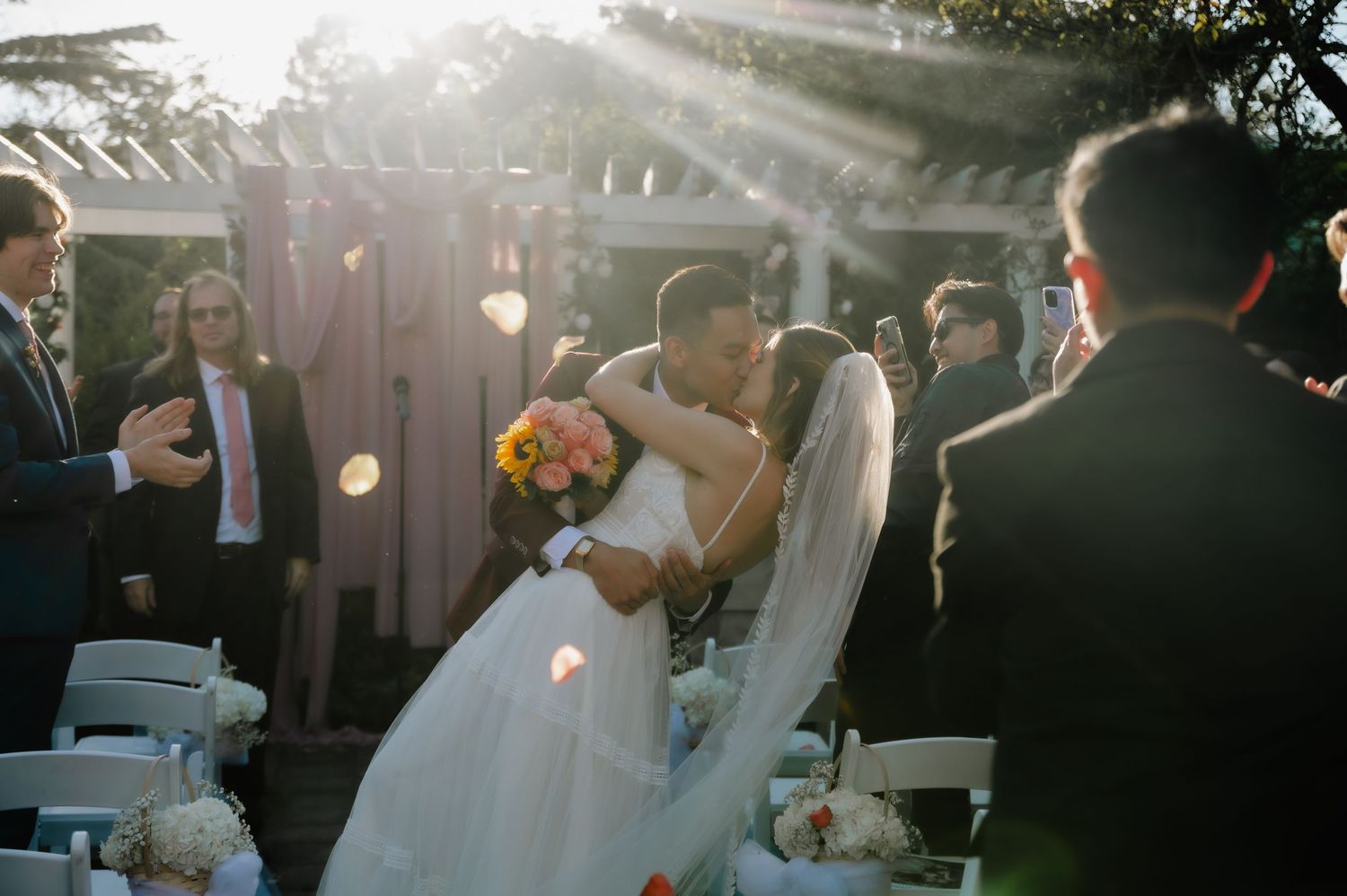 Romantic outdoor wedding scene at sunset with string lights and celebrating guests.