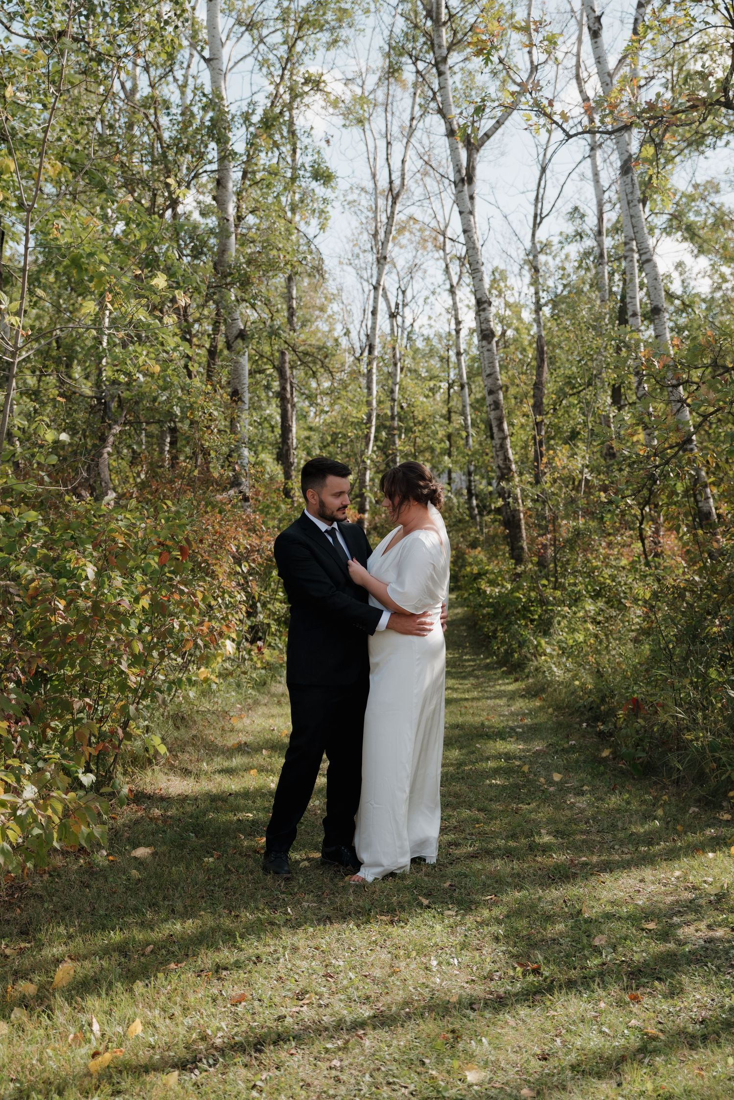 A loving couple embraces on a wooded trail surrounded by autumn trees and dappled sunlight on a fall afternoon.