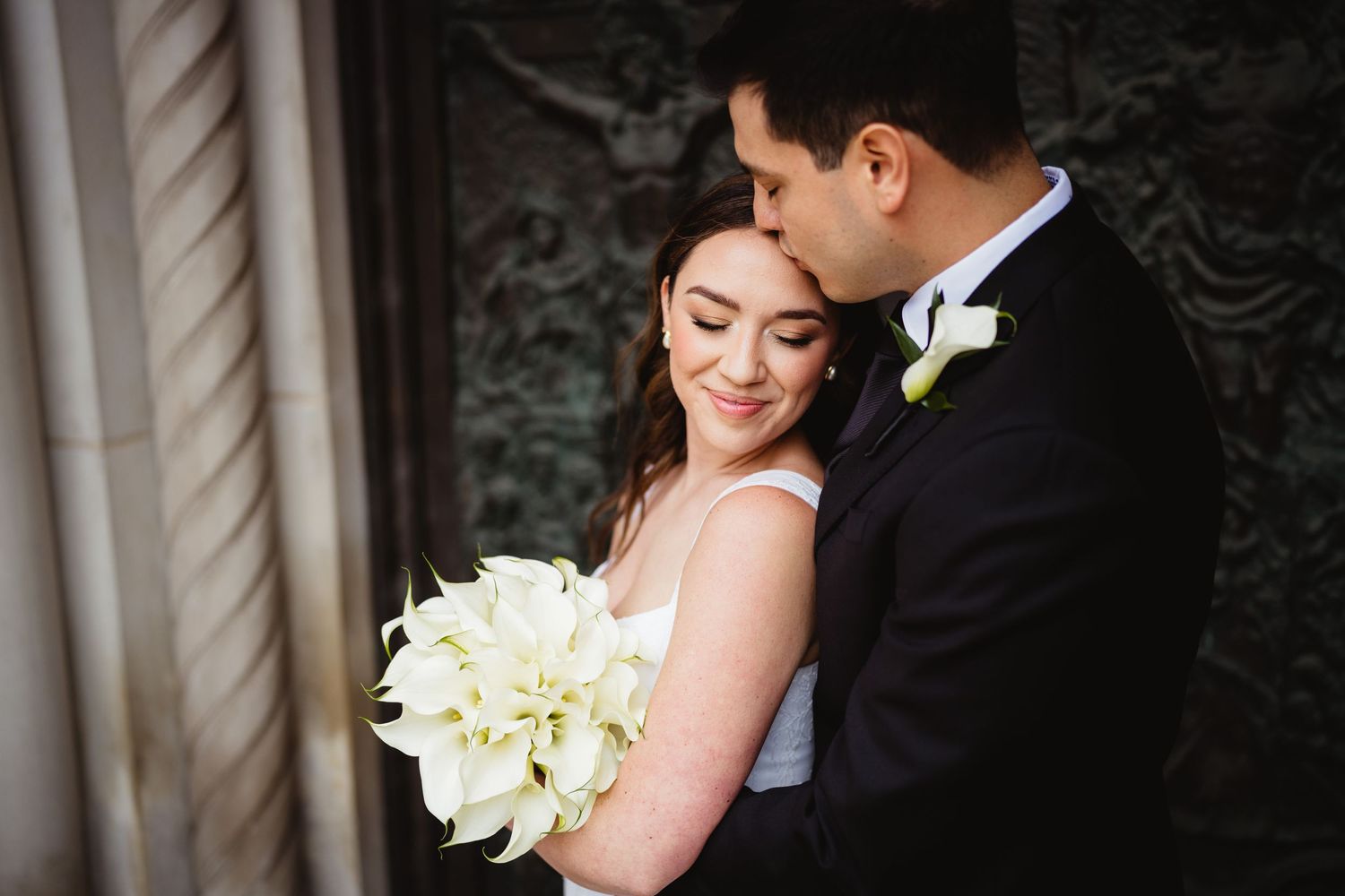 A romantic wedding moment captured with the bride holding white flowers and groom in classic black suit.