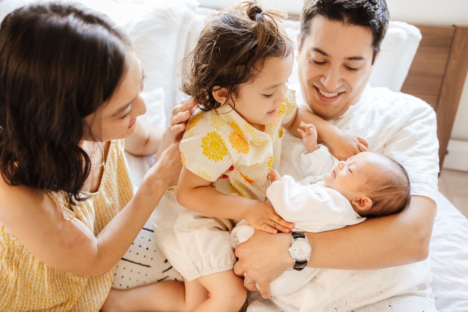 A heartwarming family moment showing parents bonding with their young baby and toddler in bed