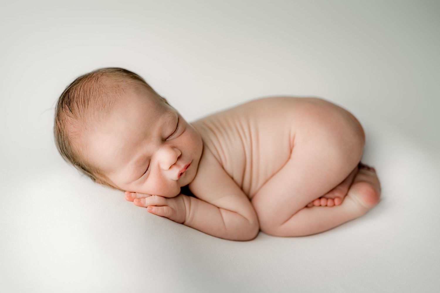 A sleeping newborn infant curled up peacefully on a white background in a fetal position.