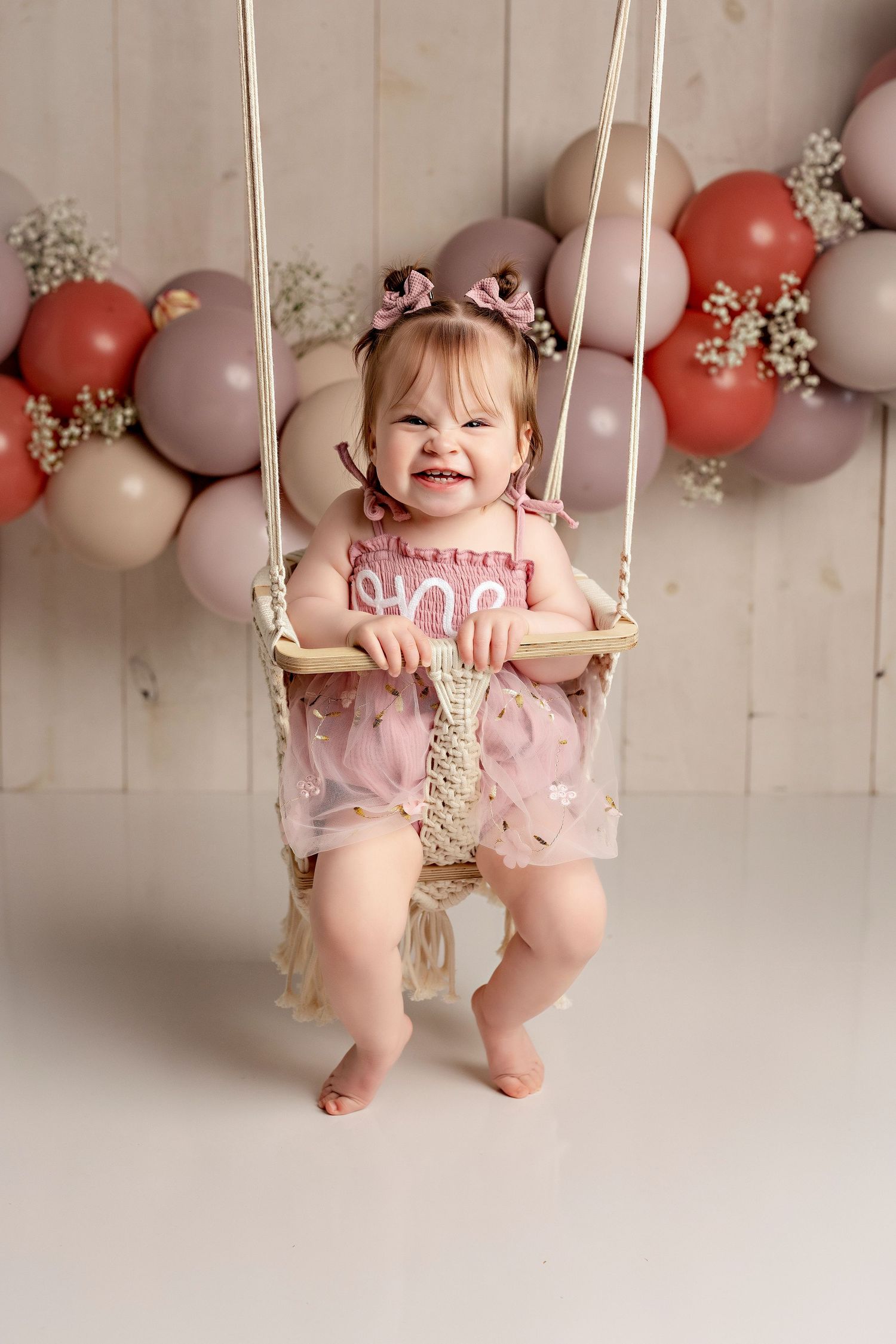 A sweet party backdrop with peach and mauve balloons frames a macrame swing with soft floral accents.