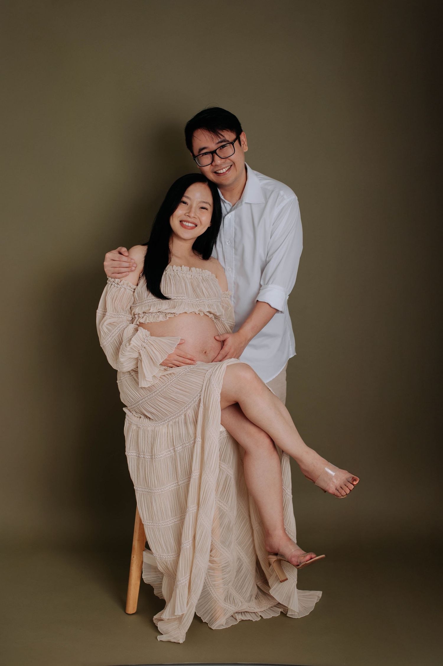 Creative maternity photo with couple seated on wooden stool in studio setting.