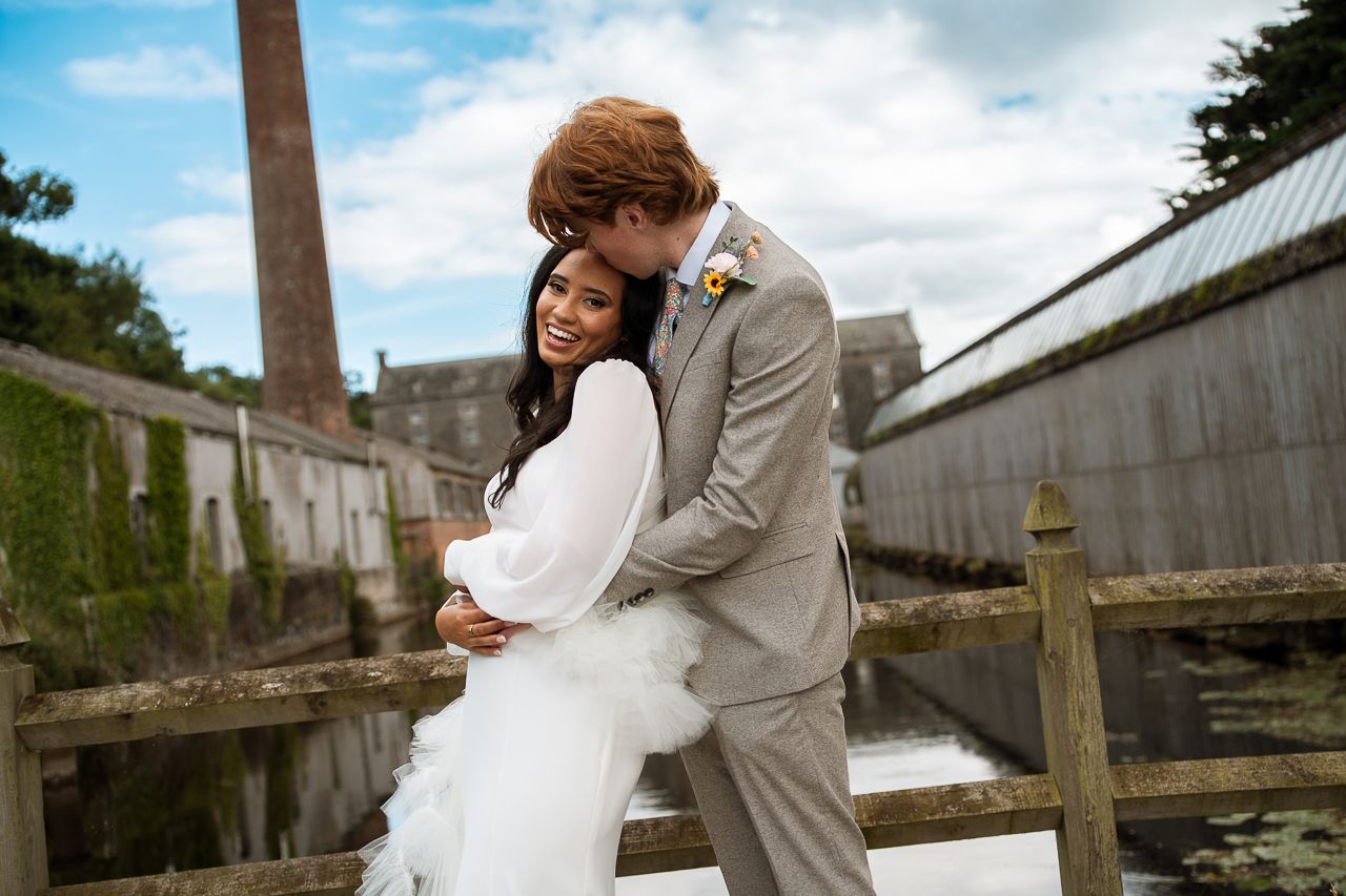 Wedding couple posing by wooden dock and rustic buildings on waterfront.