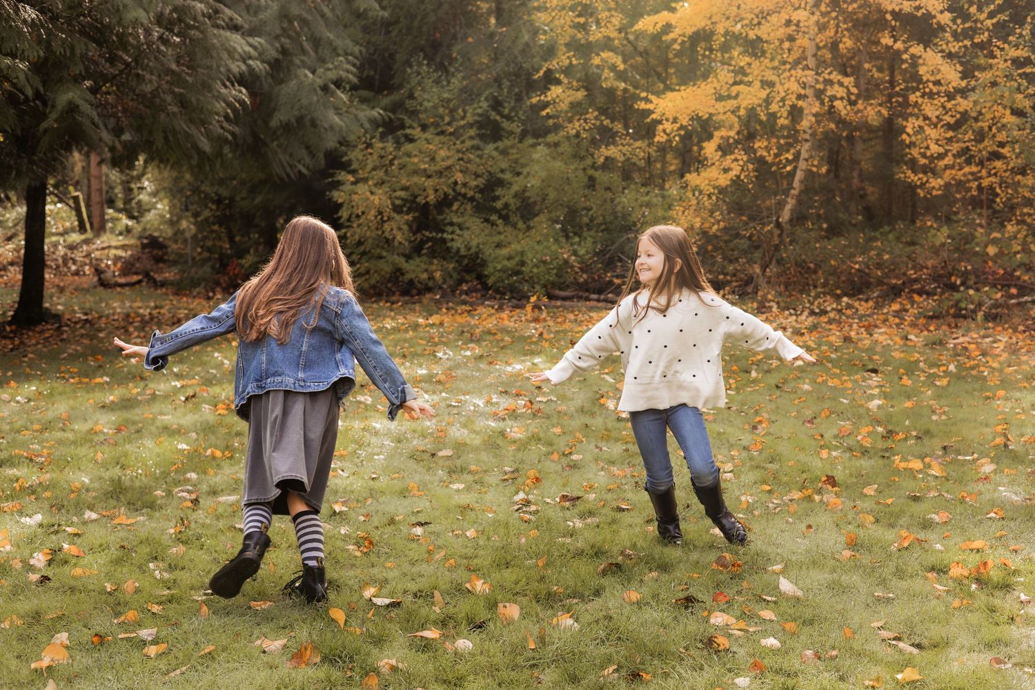 Family of four dancing outdoors in autumn park, parents spinning two young girls among colorful fall foliage.