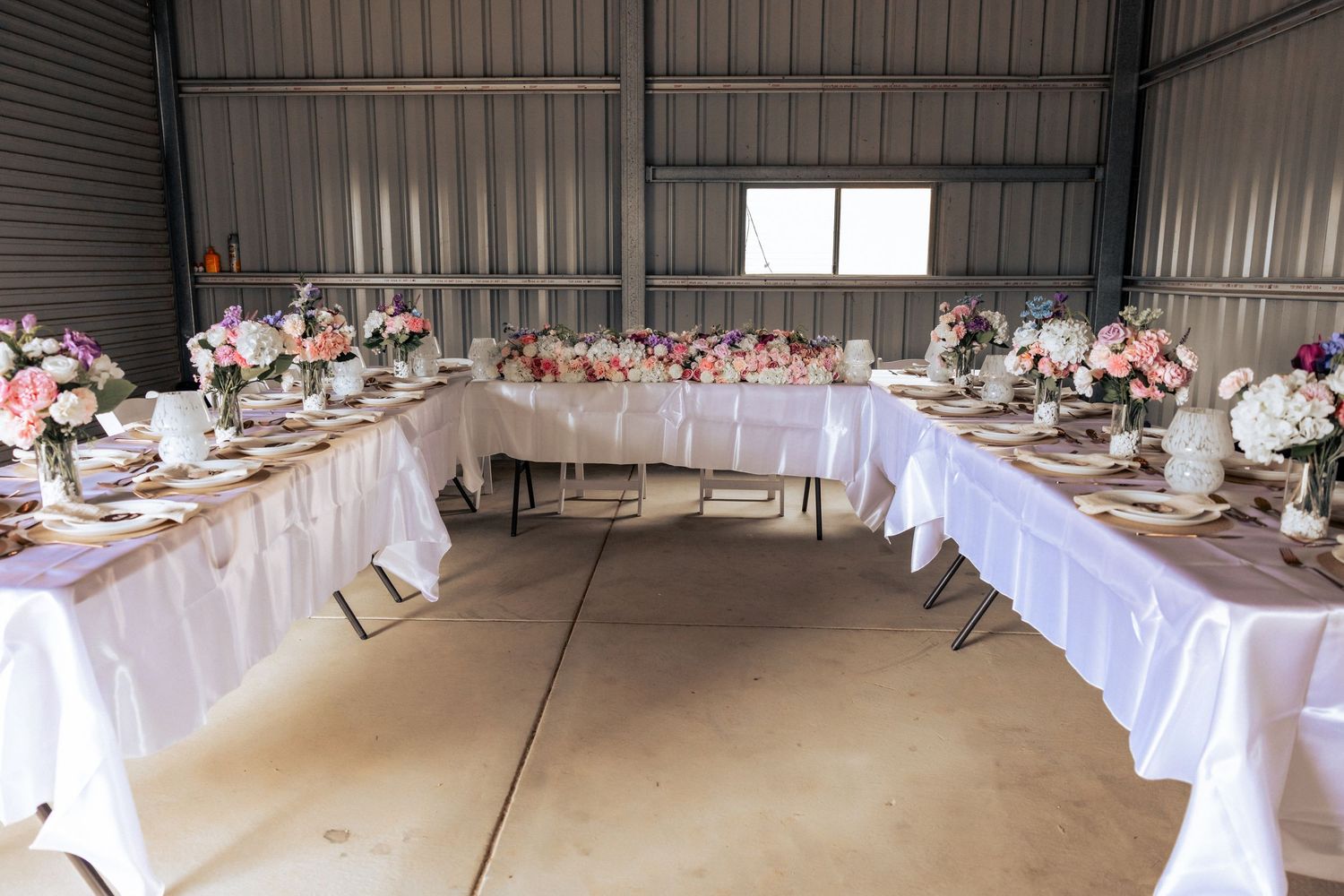 Elegant wedding reception tables with white linens and pink floral centerpieces set up inside a rustic barn venue.
