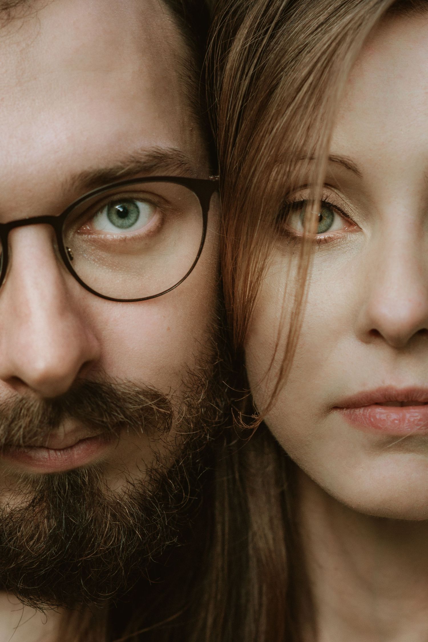 Close-up portrait of a bearded man wearing glasses and a young woman with blonde hair, both with green eyes.
