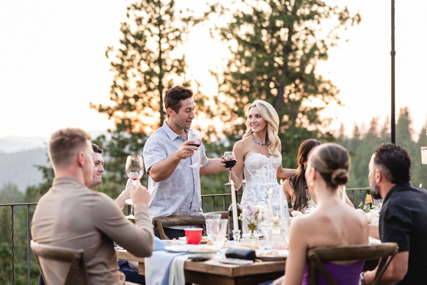 Couple raising wine glasses in a toast with friends at a sunset outdoor dinner party.