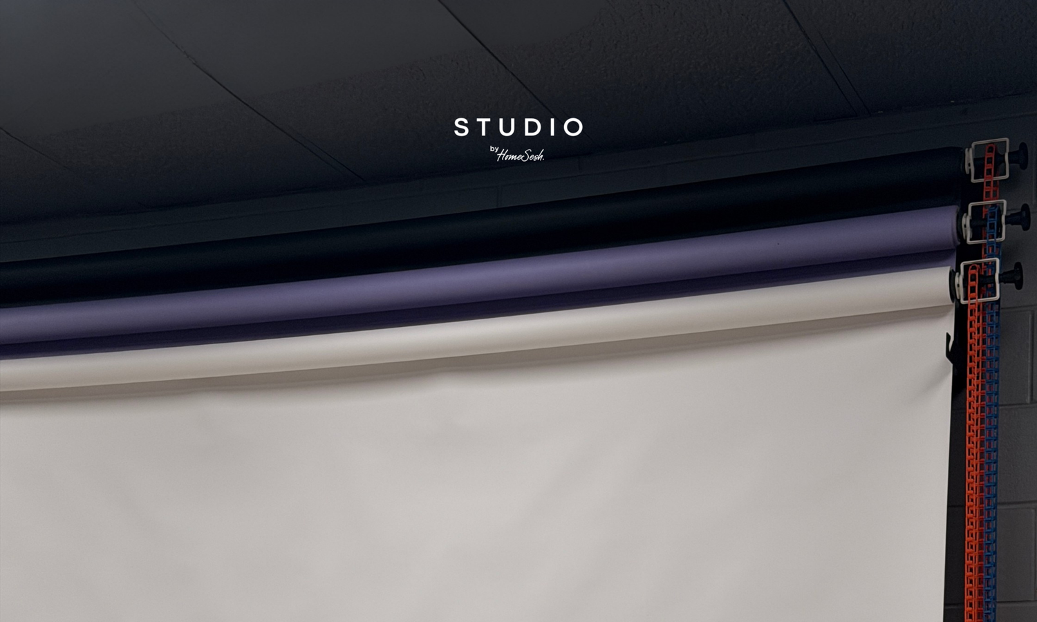 A minimalist gray backdrop with 'New Space Same Warmth' text in elegant serif font, featuring a purple rail and orange strap.