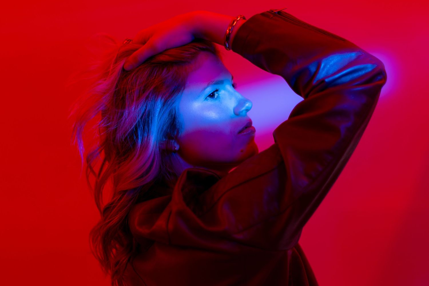 Silhouette figure illuminated by dramatic red and blue lighting poses with hand raised against vibrant background.