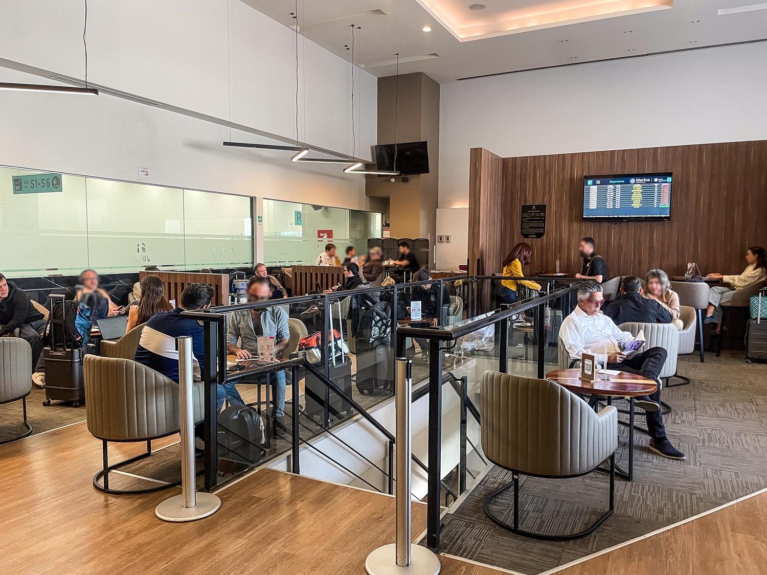 Modern airport lounge interior with glass partitions, wooden walls, and travelers seated at various workstations.