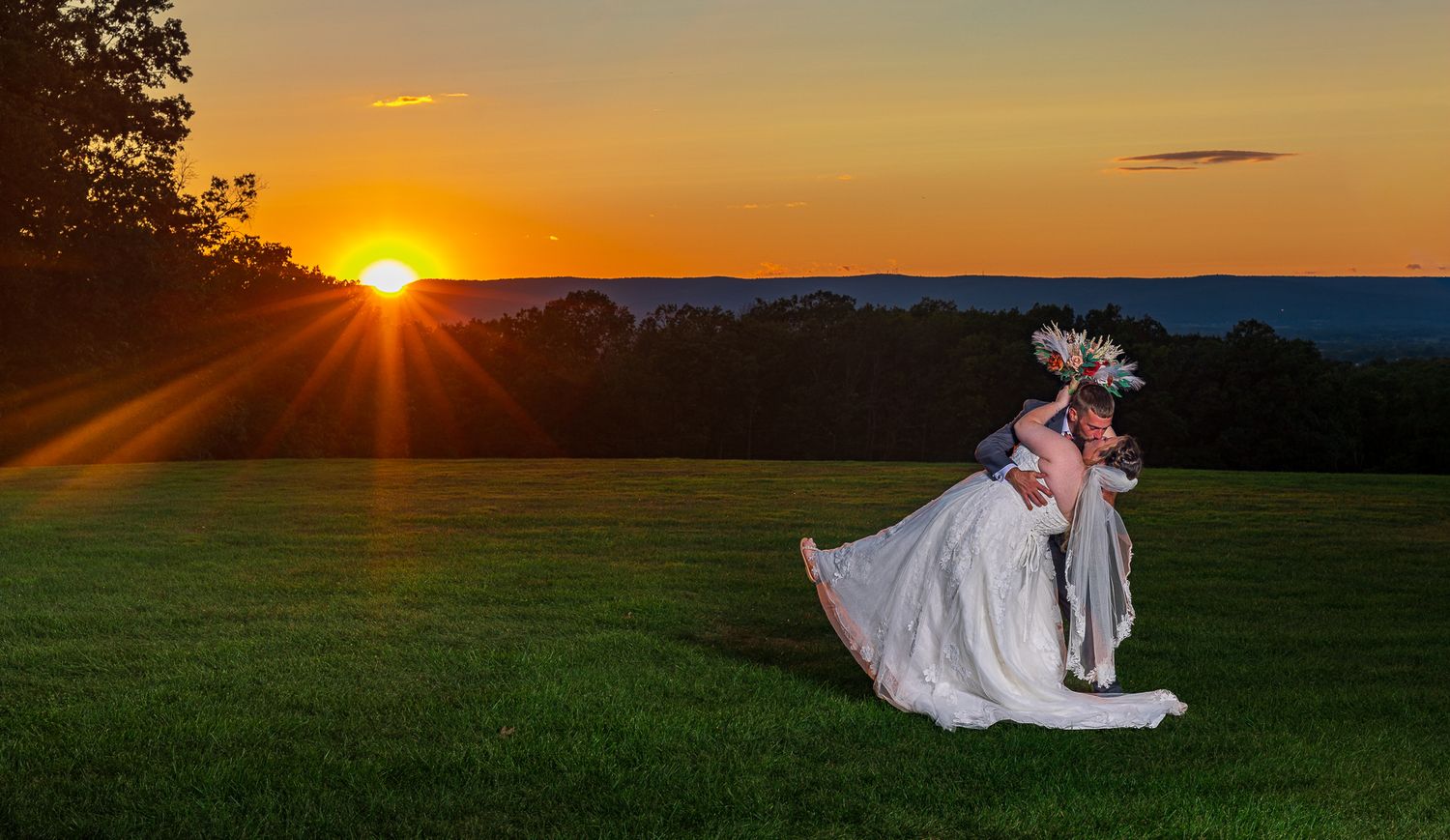 Newlyweds embrace outdoors with red brick building and autumn foliage in background.