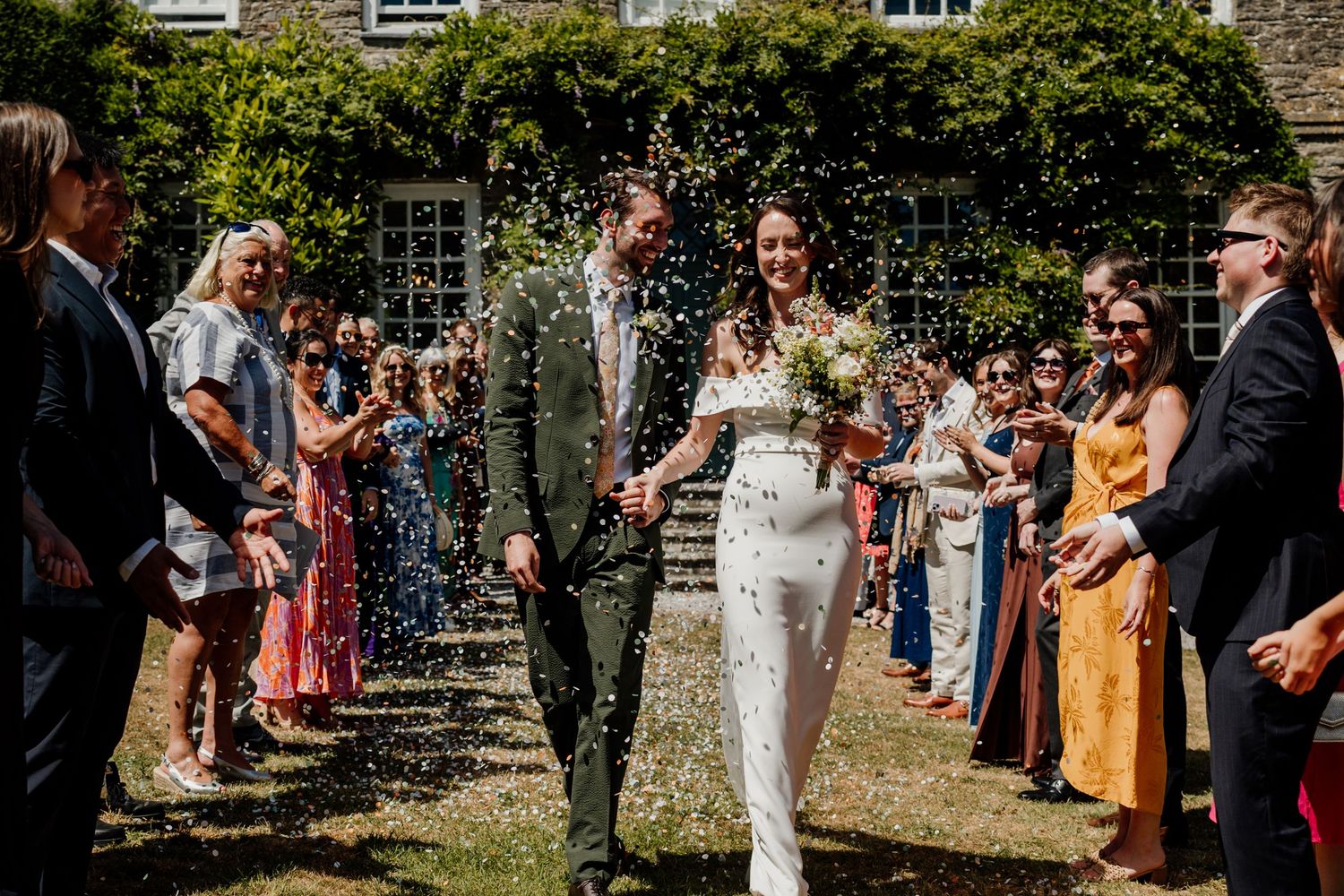 Bride and groom walk through confetti shower in the garden at Kingston Estate in Devon.