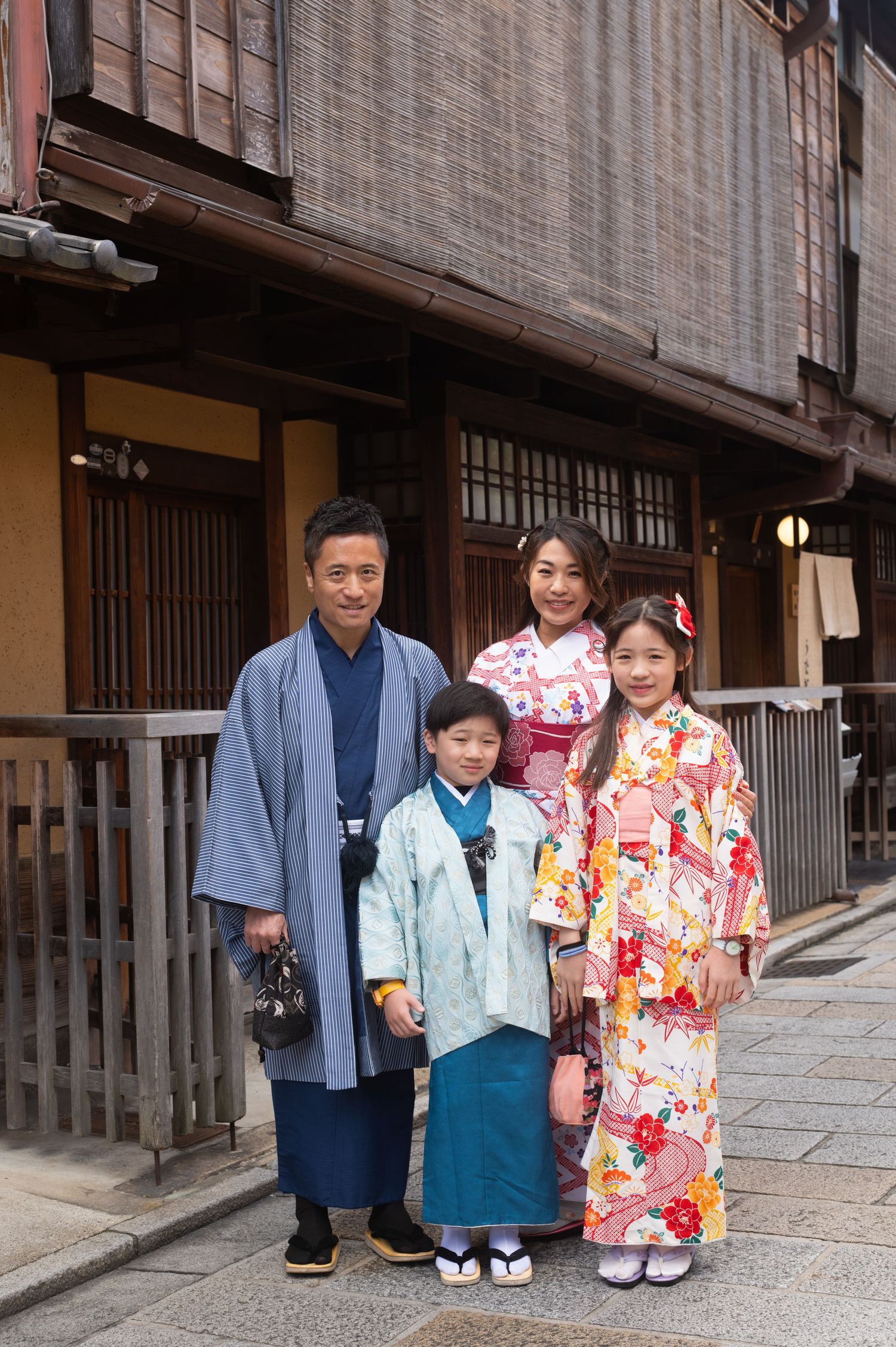 Family of four wearing traditional Japanese kimono and hakama posing in Kyoto Gion historic district.