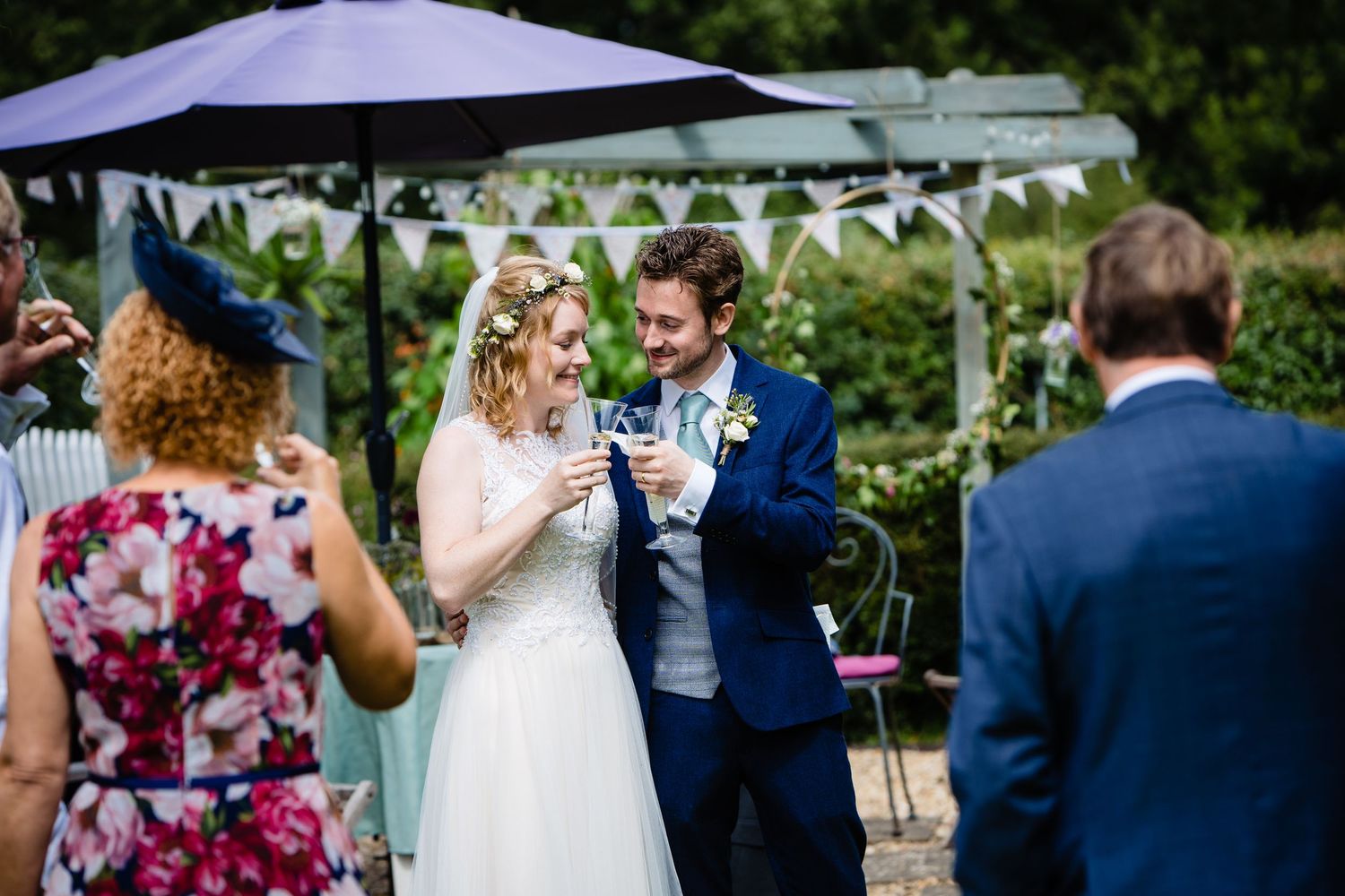 Bride and groom toasting champagne glasses outdoors at backyard wedding reception with bunting decorations.