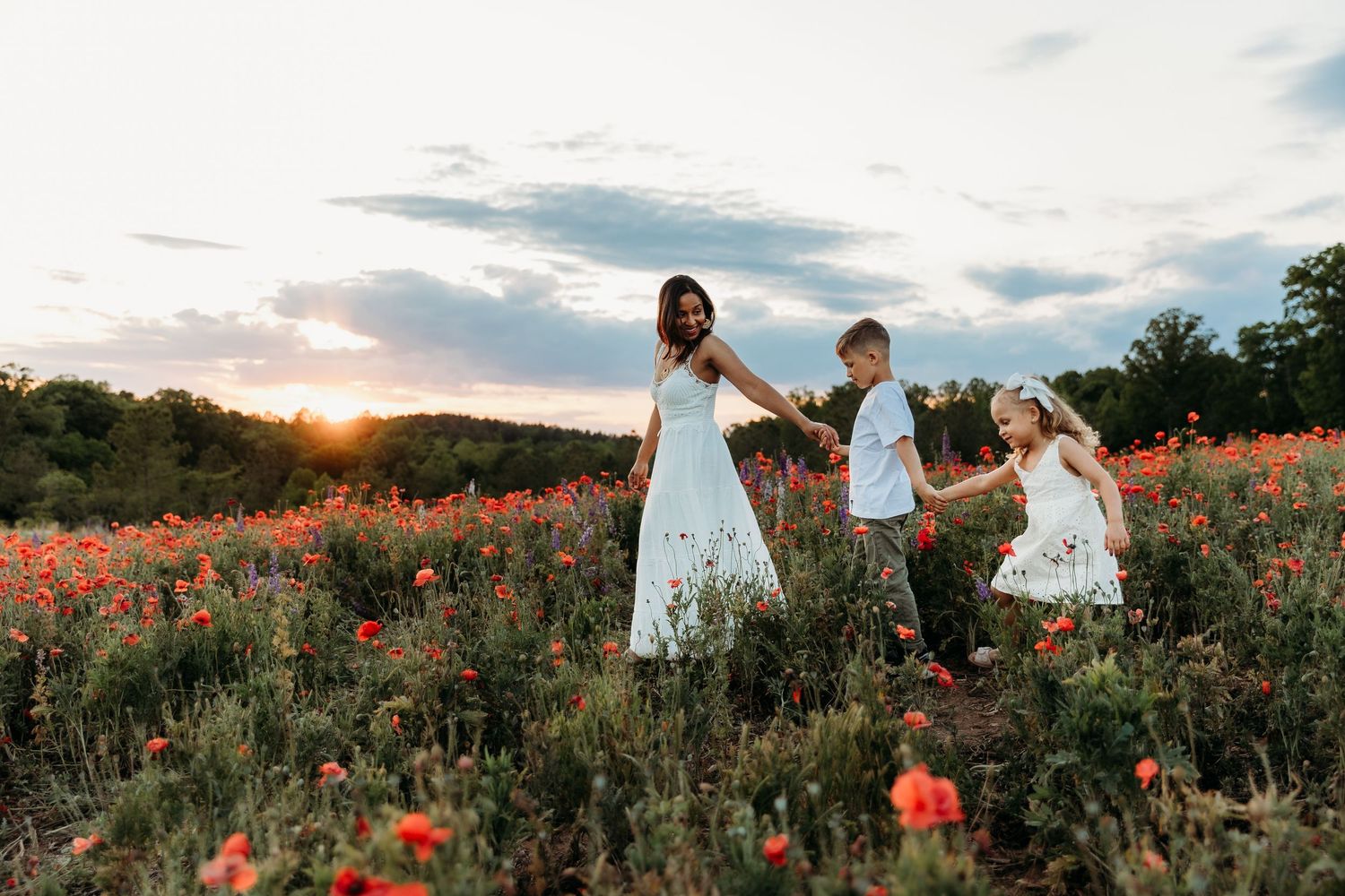 Family embracing in a vibrant poppy field at golden sunset, wearing white outfits amid red wildflowers.